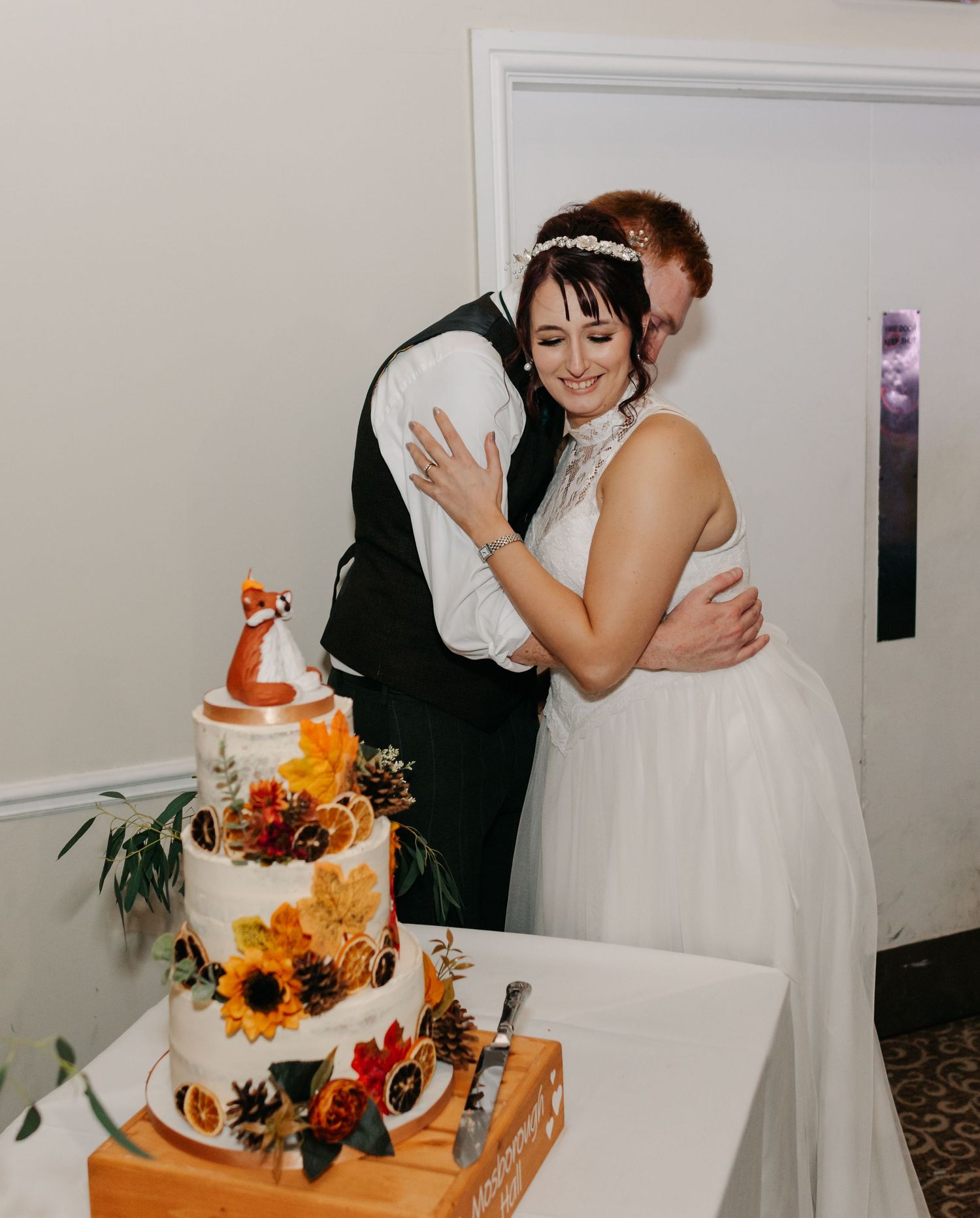 Newlyweds sharing an intimate moment beside their autumn-themed wedding cake.