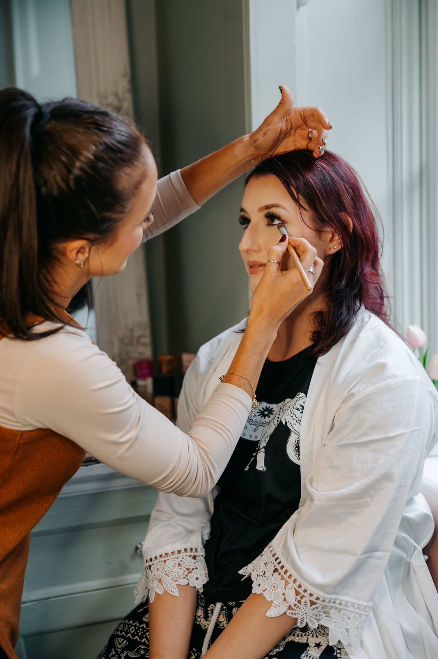 Wedding makeup artist applying cosmetics to a client wearing a white lace top.