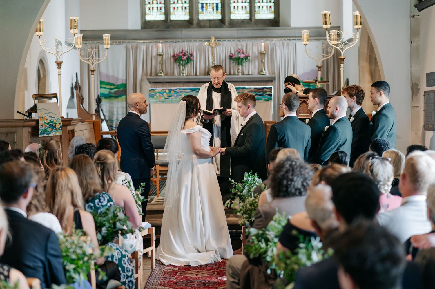 Wedding ceremony in a beautiful church with stained glass windows and wooden pews.