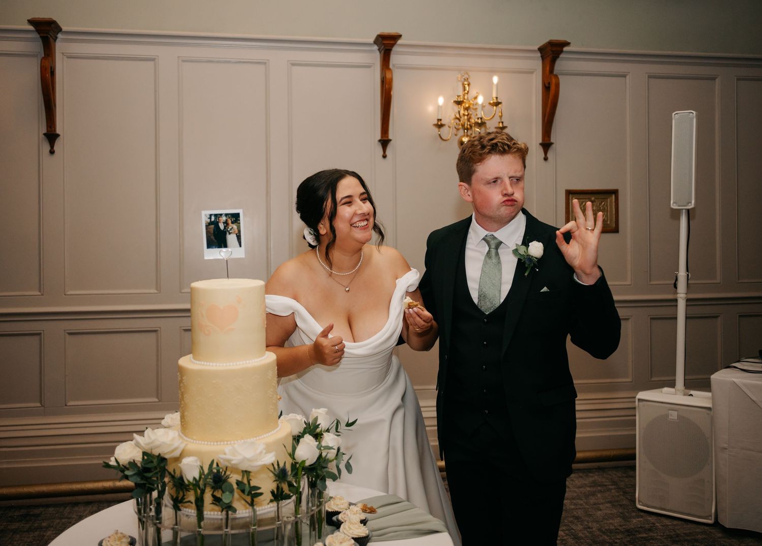 Newlyweds share a playful moment while cutting their elegant white wedding cake at the reception.