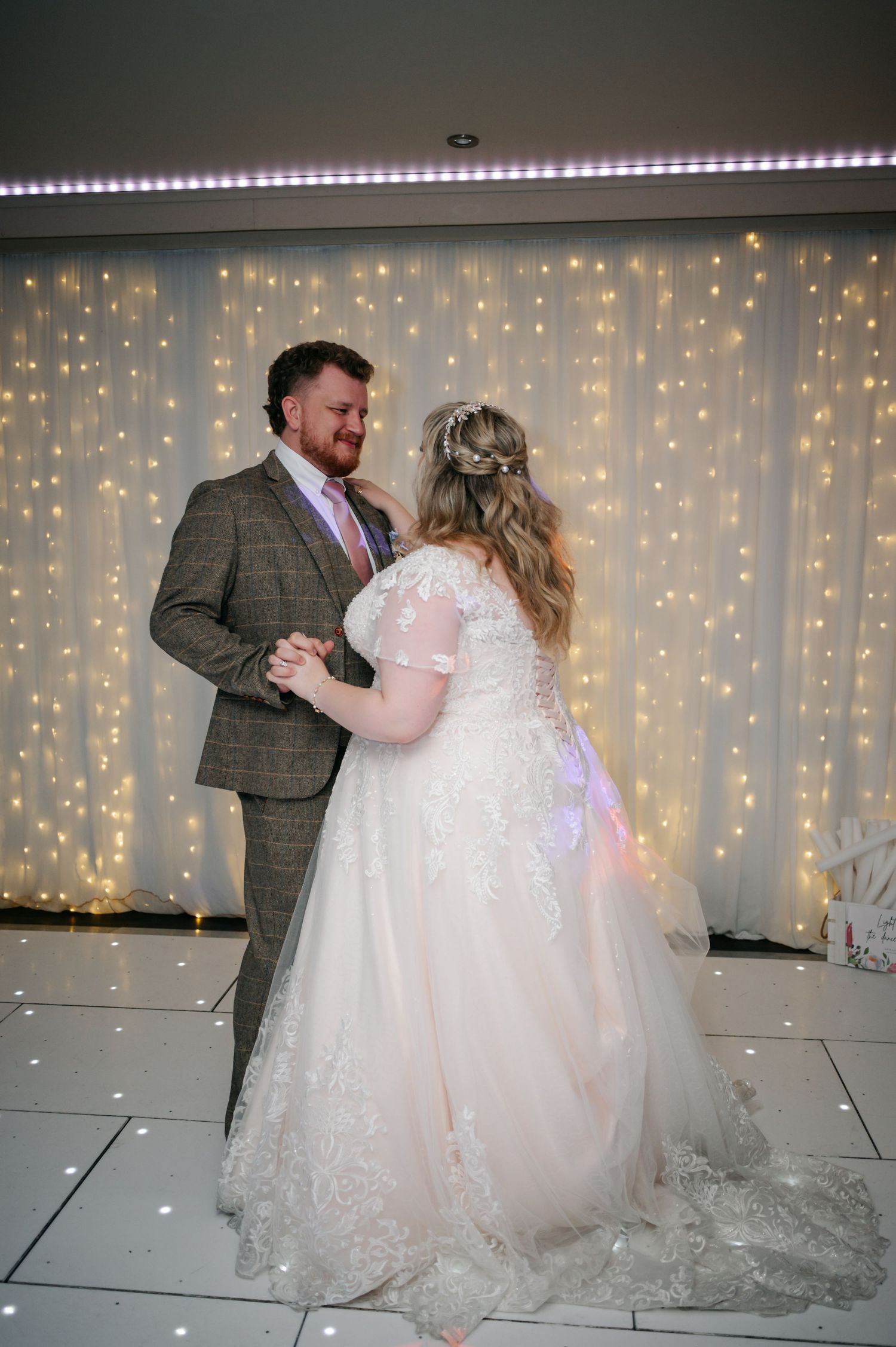 Bride and groom share their first dance in front of a sparkling fairy light backdrop at their wedding reception.
