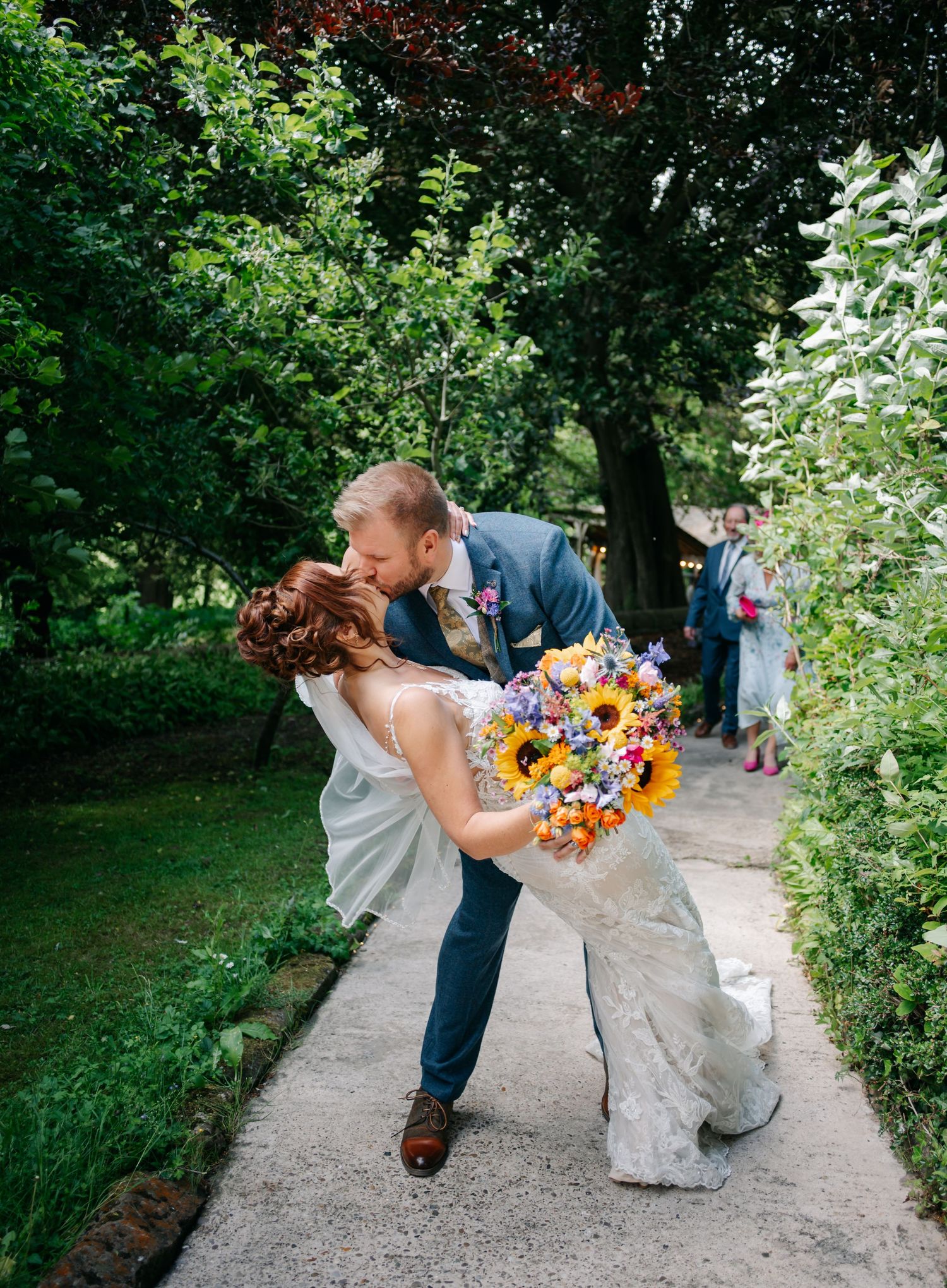 A romantic dip kiss on a garden pathway surrounded by lush greenery.