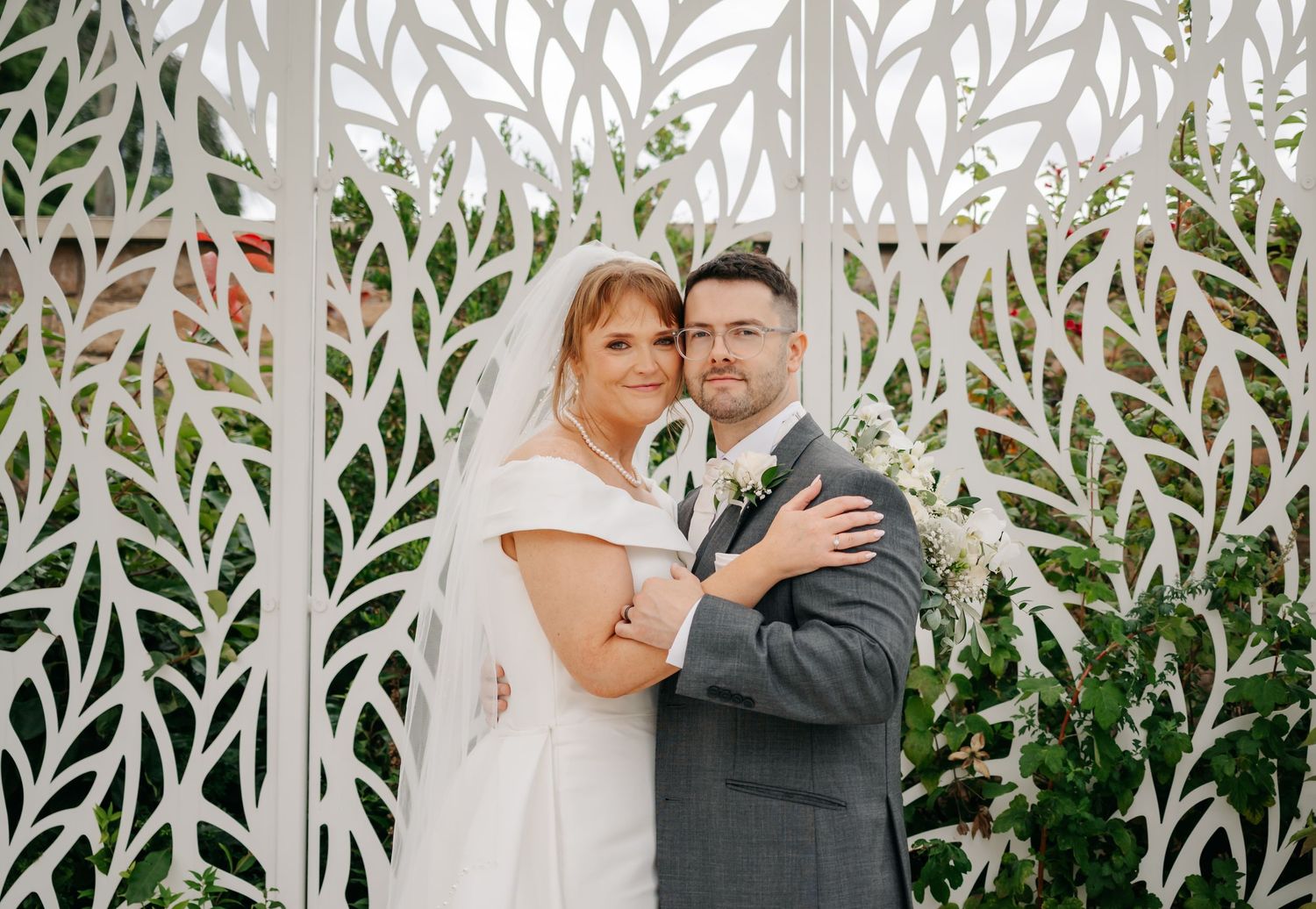 Wedding couple sharing a moment under decorative white leaf-patterned pergola.