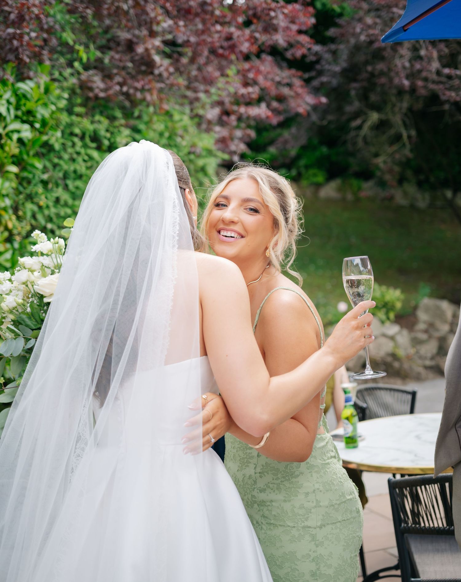 Wedding guests celebrate outdoors in a garden setting with champagne glasses.