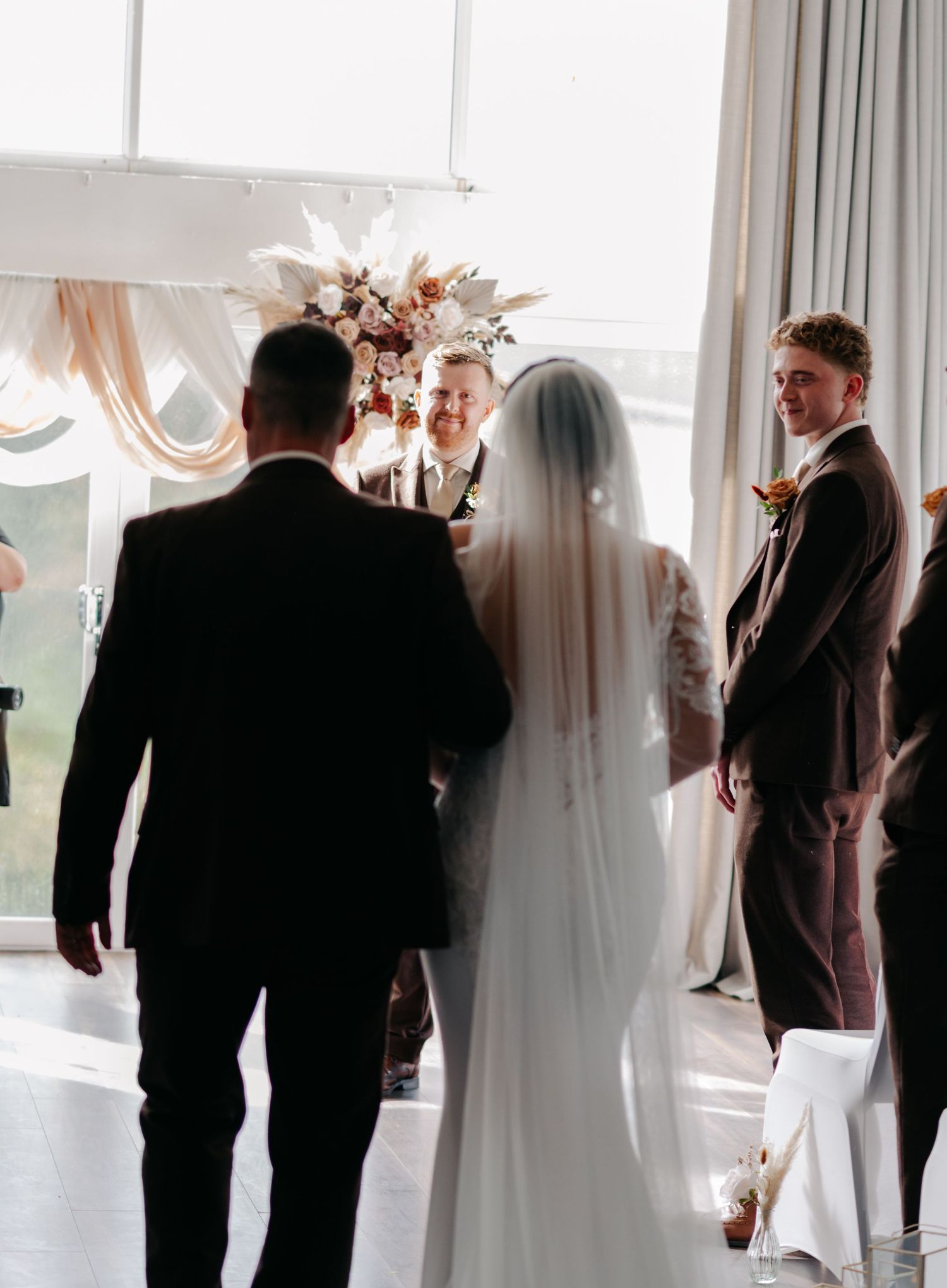Wedding guests mingling in an elegant white reception room with sheer curtains and natural lighting.