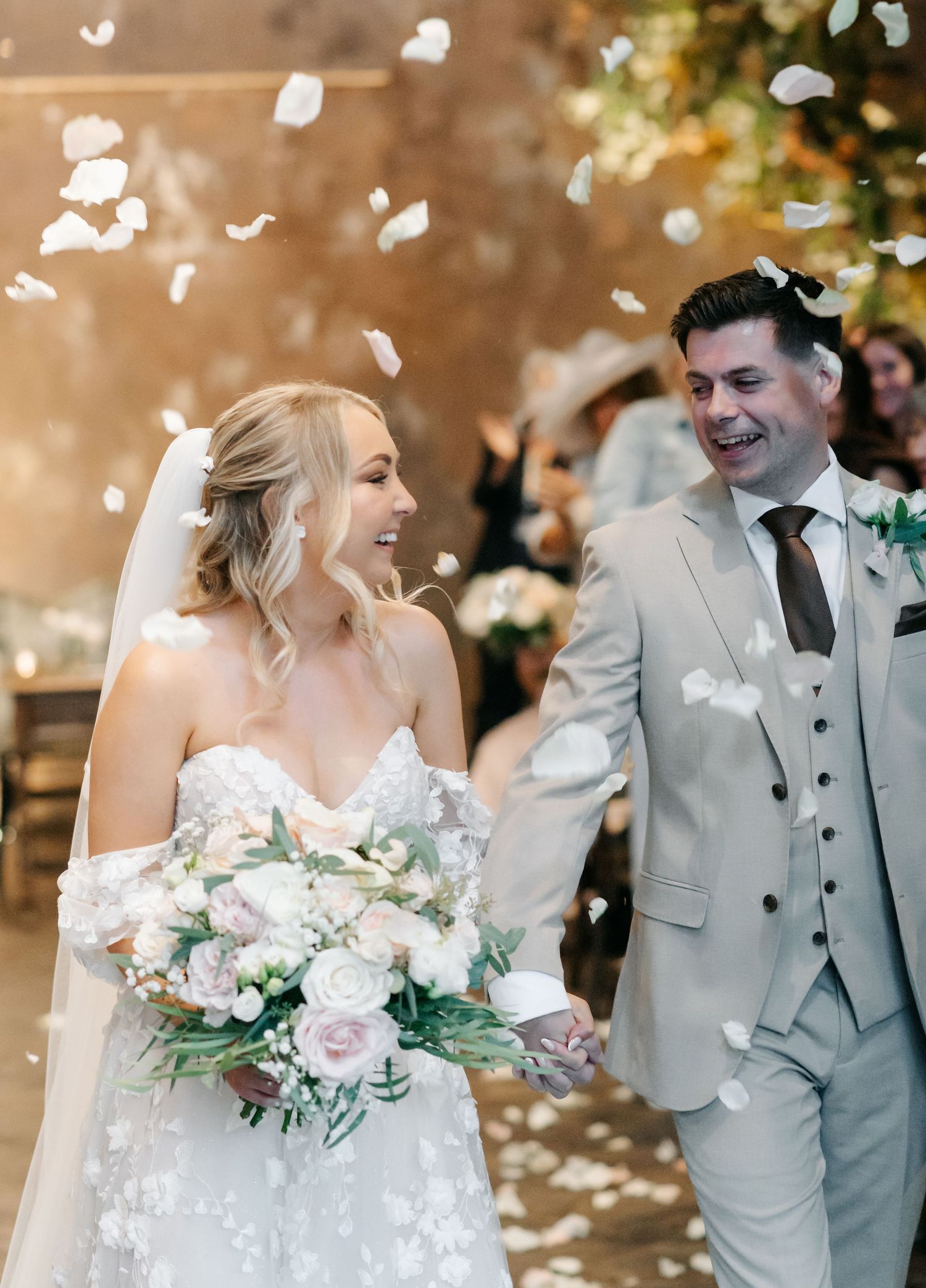 Joyful wedding couple celebrating with confetti and white flowers.