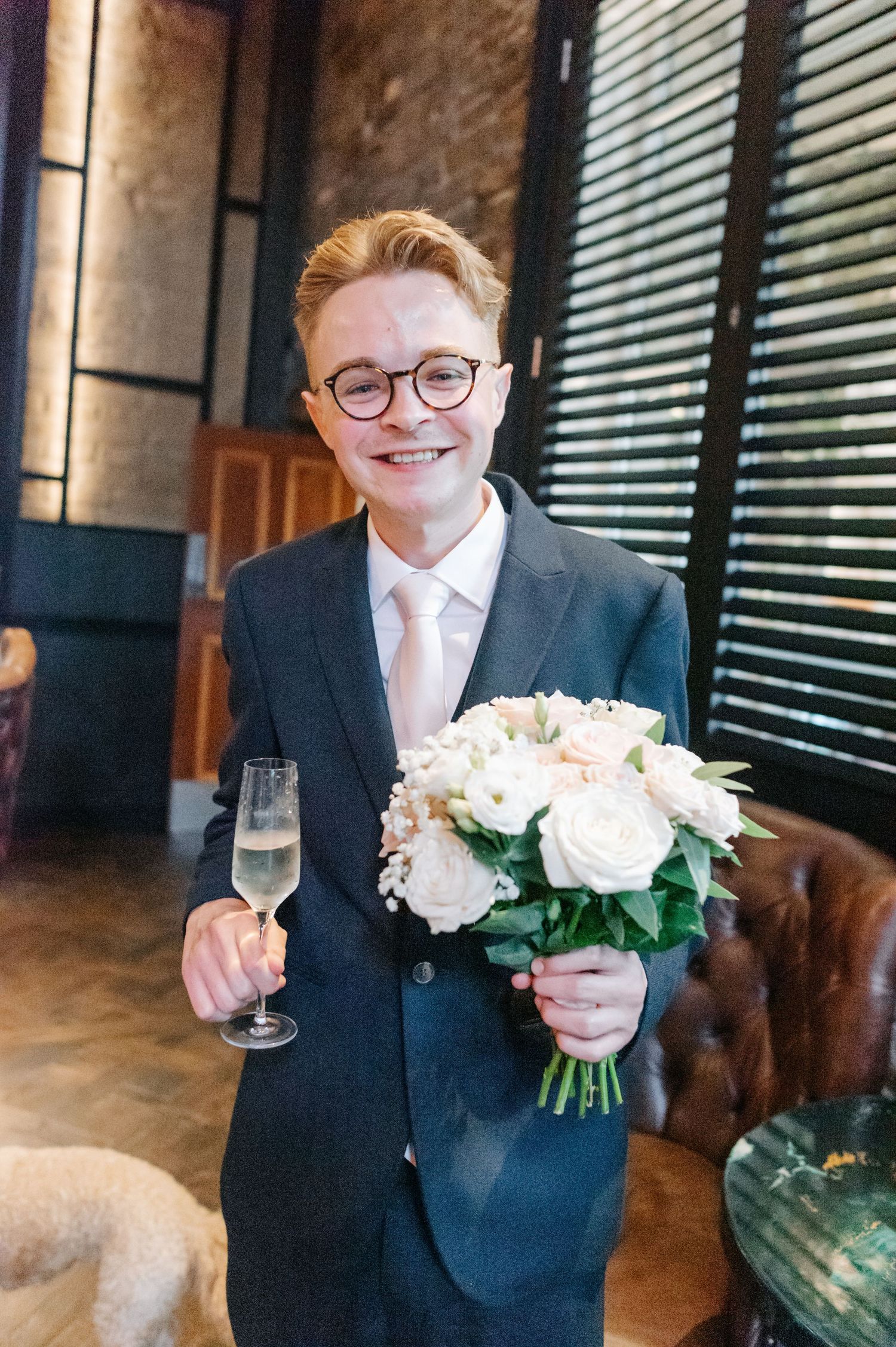 Wedding party member in navy suit holding delicate pink and white rose bouquet.