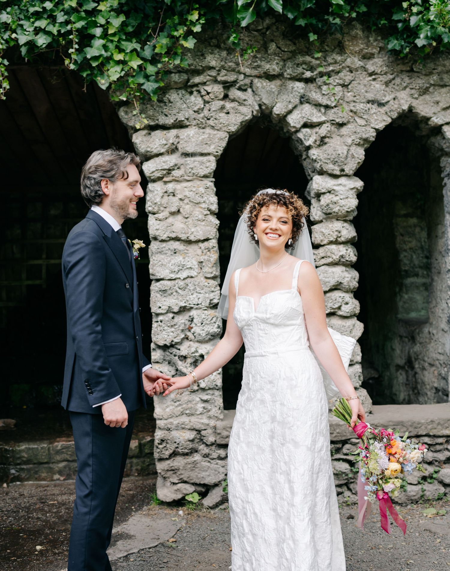 A couple shares candid moments against a rustic stone wall backdrop during their wedding.