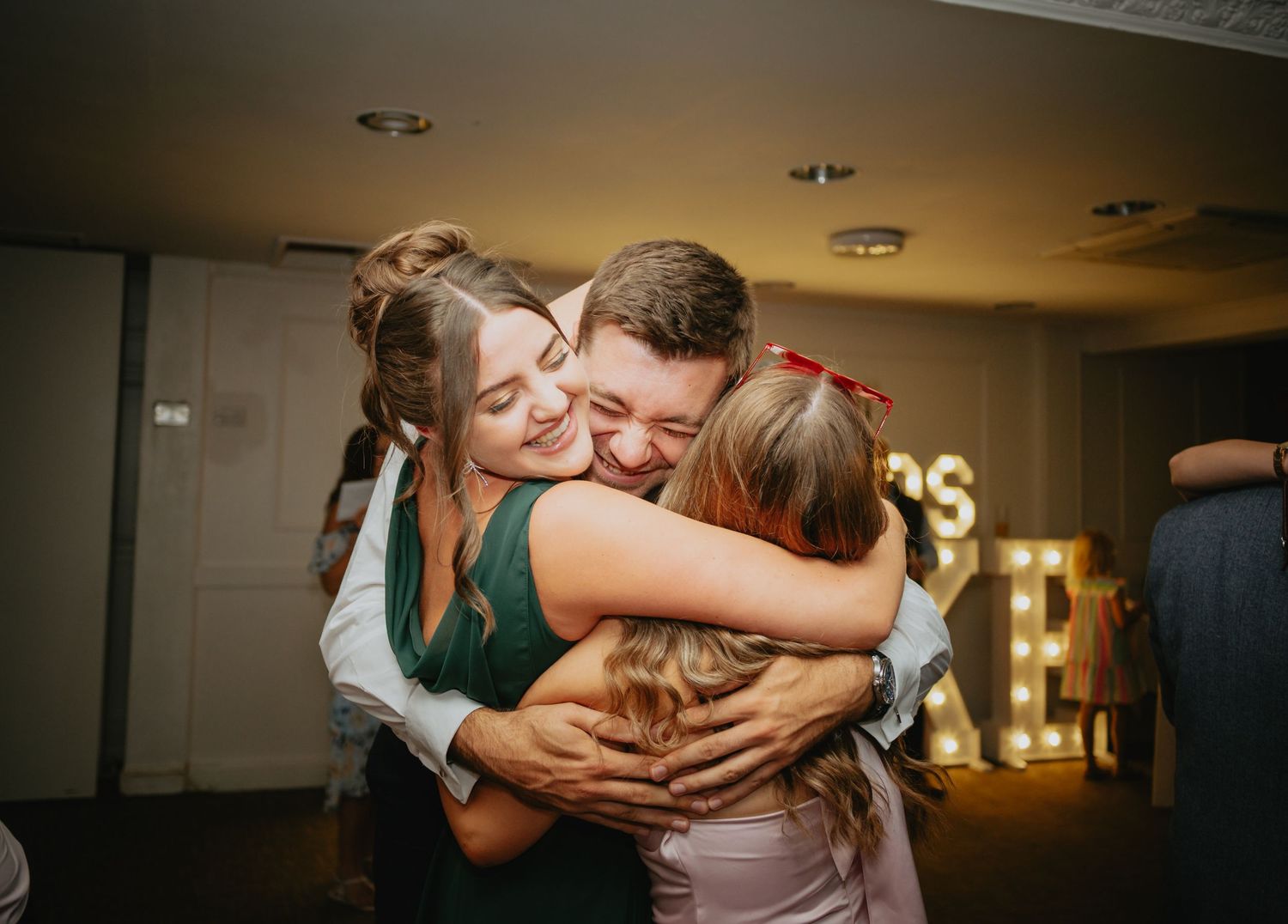 Emotional embraces shared during dimly lit wedding reception.