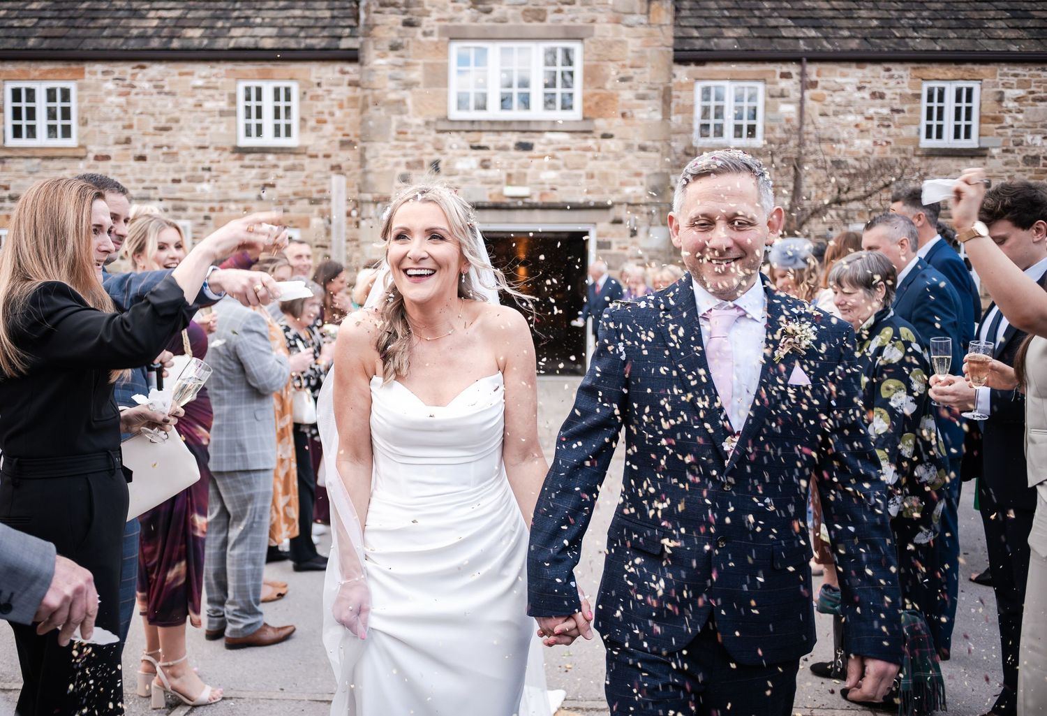 Guests celebrating with confetti toss outside stone building at wedding reception.