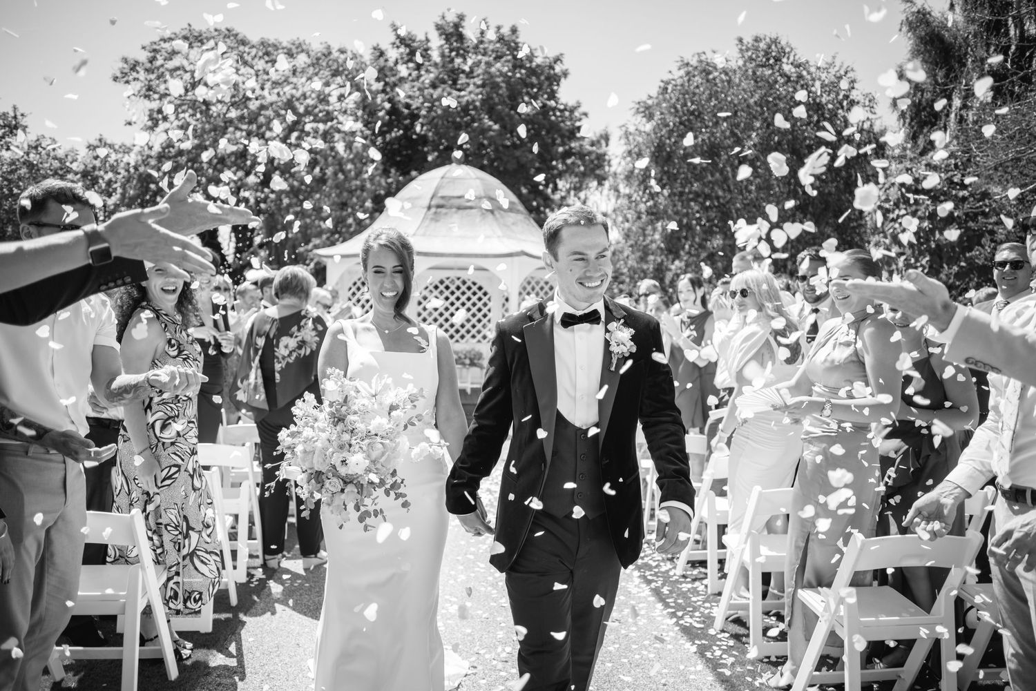 Wedding guests showering couple with confetti outdoors during daytime celebration.