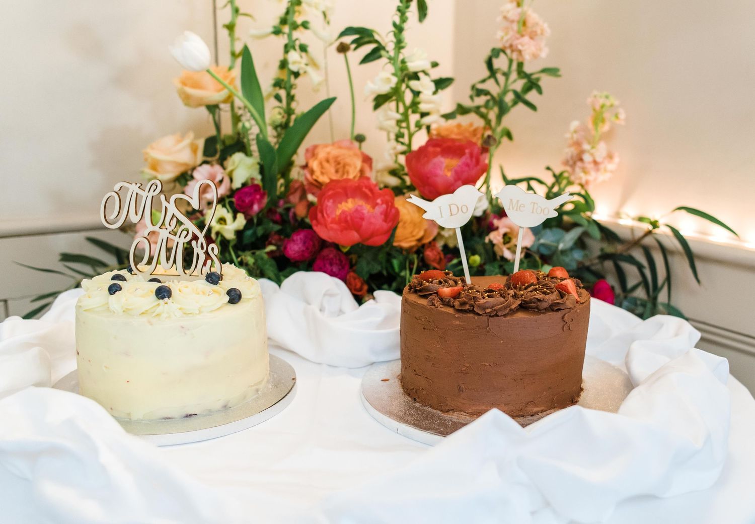 White and chocolate wedding cakes displayed with colorful floral arrangements.
