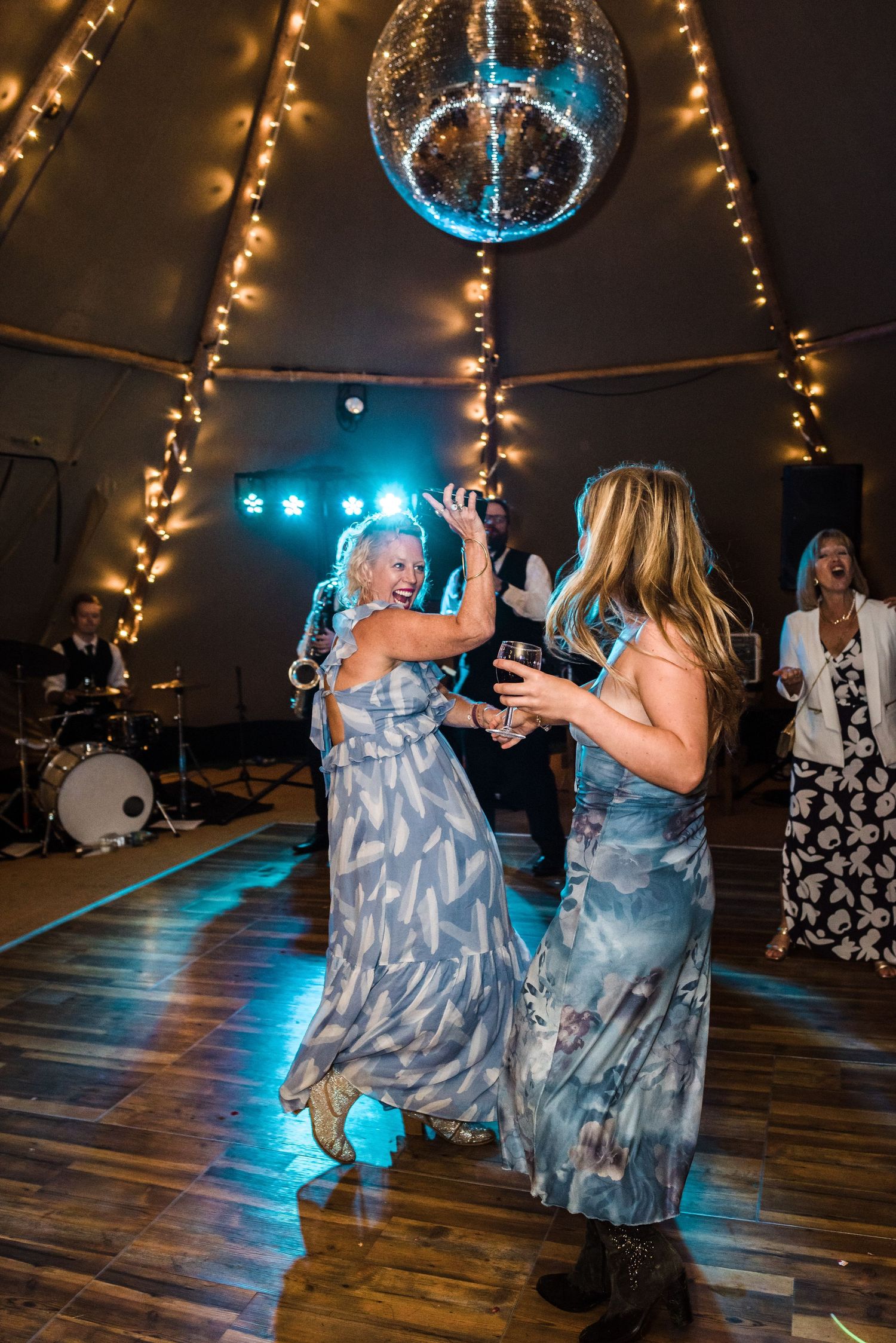 Two guests dancing under a disco ball with string lights in wedding tent.