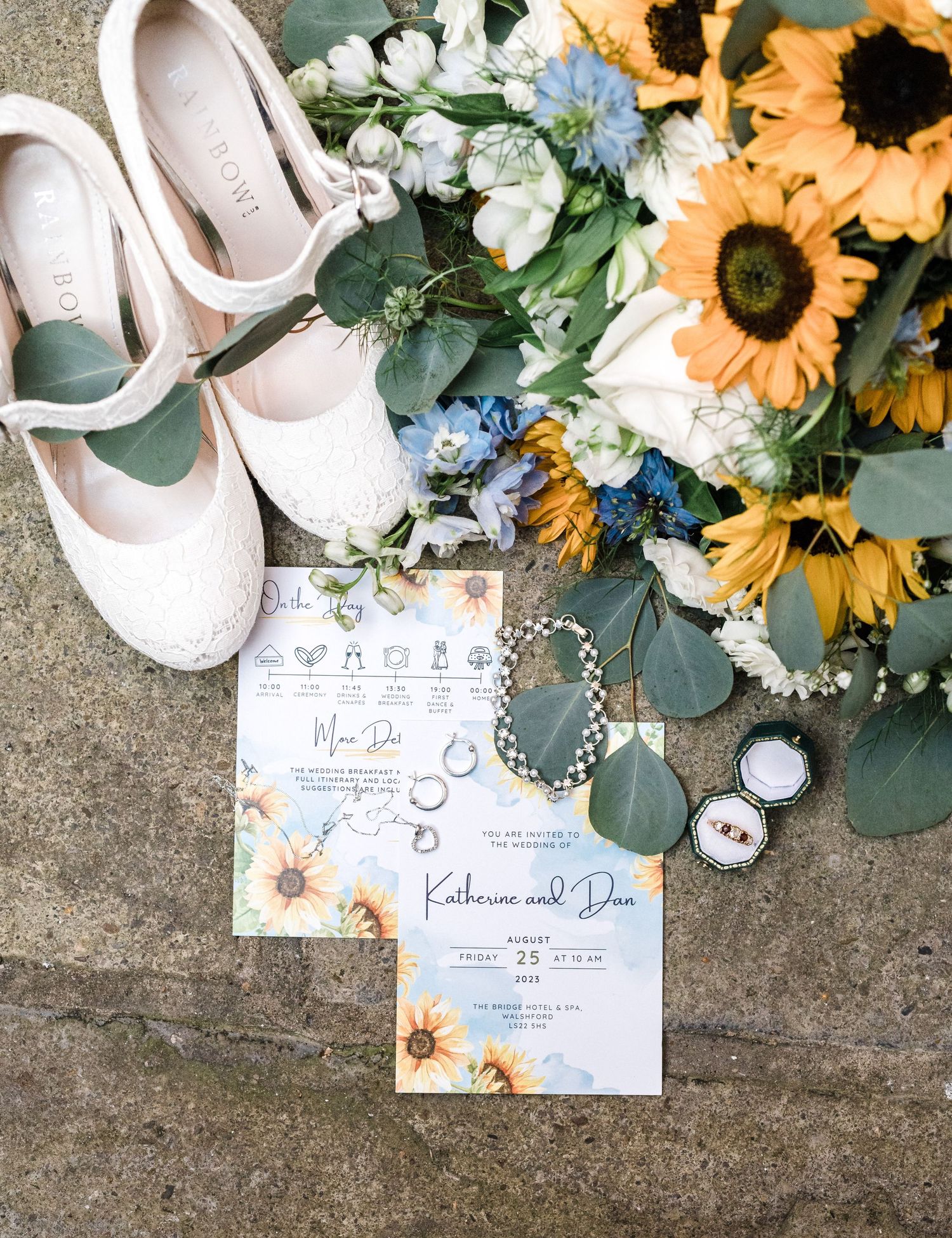 Wedding details including white shoes, sunflower bouquet and floral invitation card on concrete background.