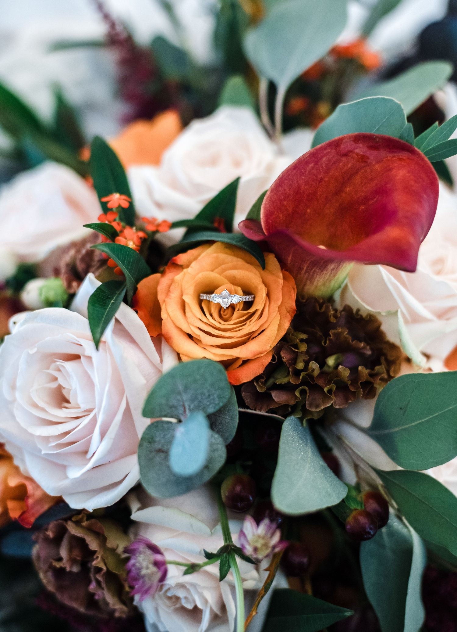 Close-up of a wedding bouquet with orange and pink roses, featuring an engagement ring nestled in a flower.