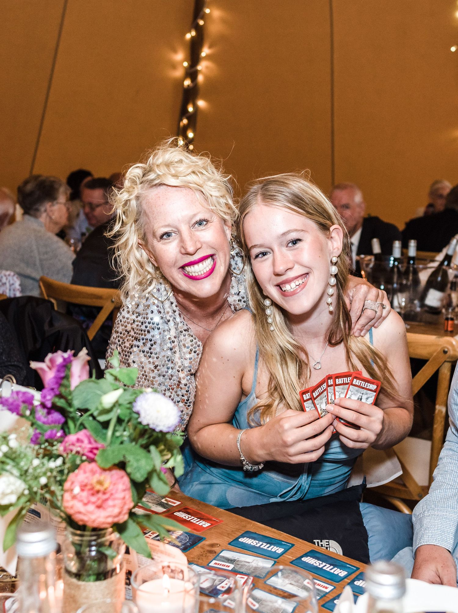 Friends playing card games at a wedding reception table decorated with flowers.