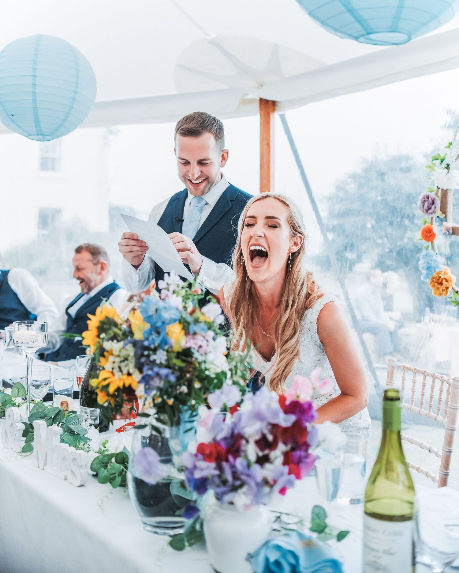Wedding celebration with laughter at a decorated table with colorful floral centerpieces.