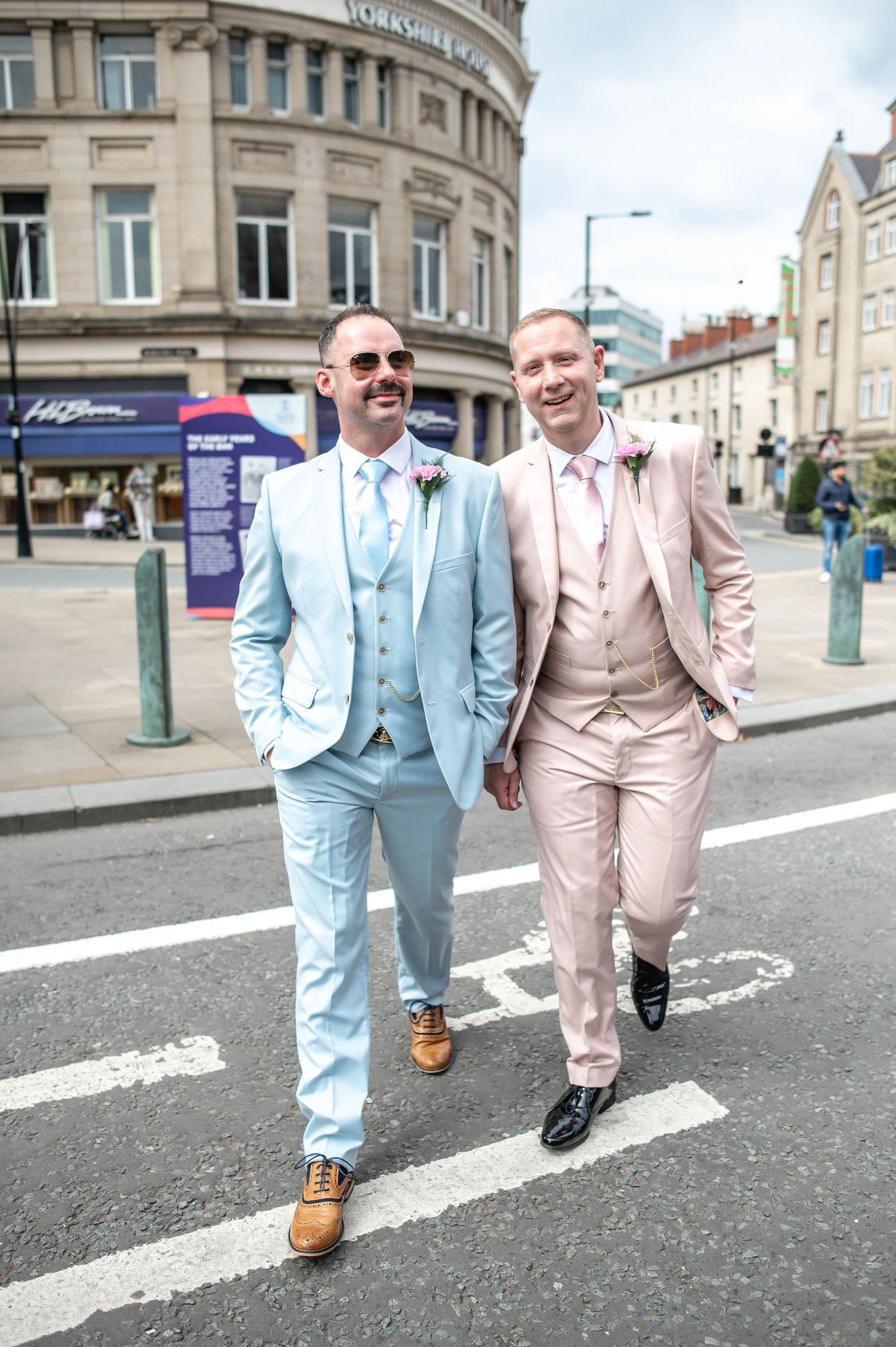 Two people in pastel suits walking together on a city street.