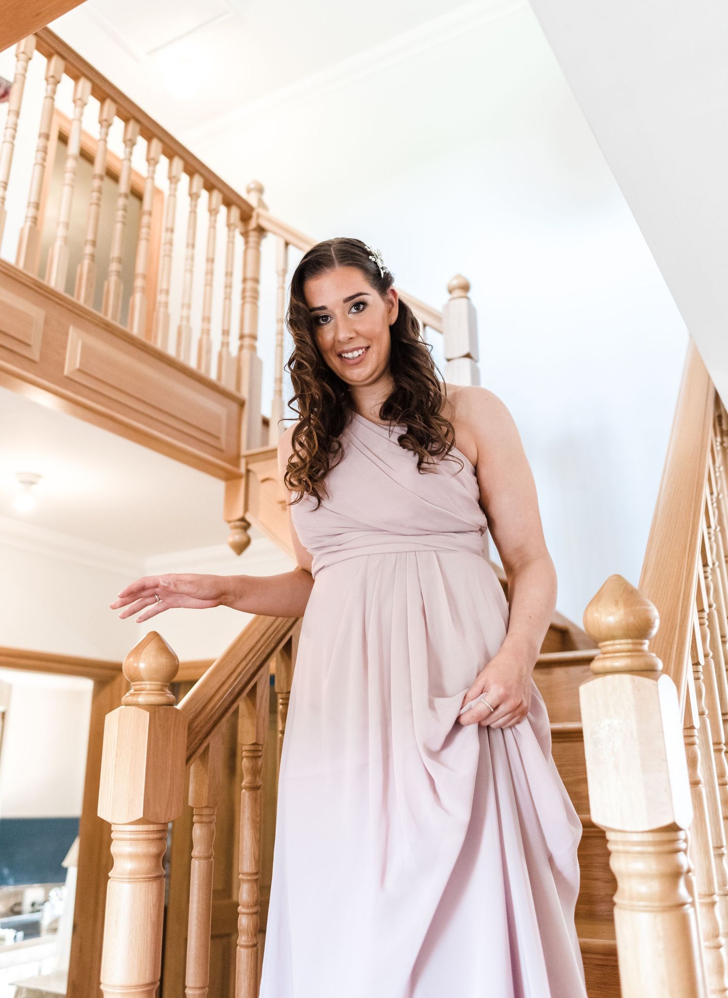 Person in pale pink bridesmaid dress poses joyfully on wooden staircase.