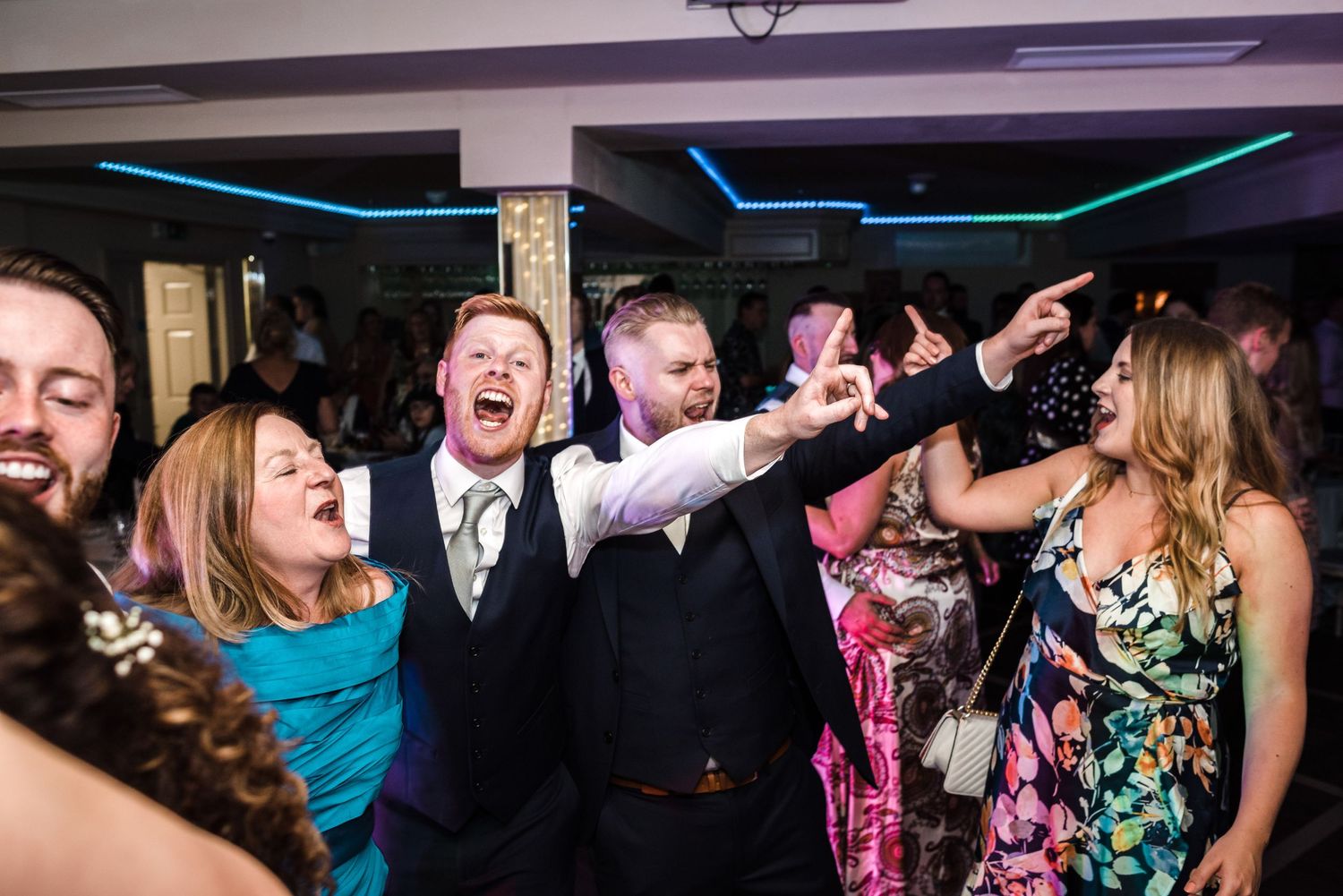 Party guests dancing and celebrating enthusiastically at a wedding reception.