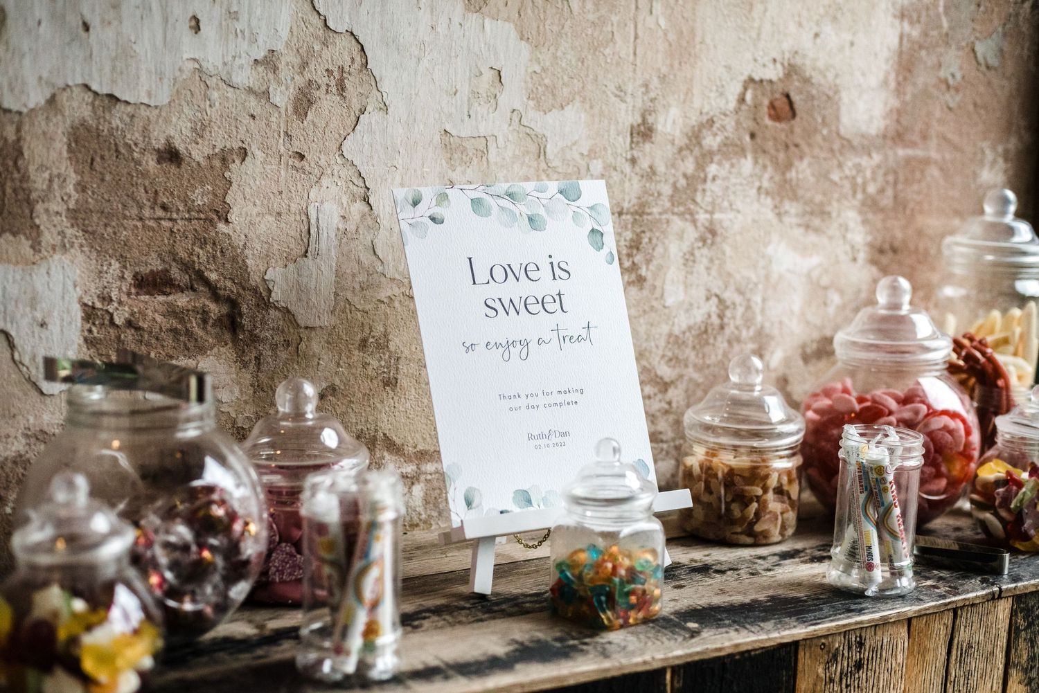 Vintage candy bar setup with glass jars and rustic signage against weathered wall.