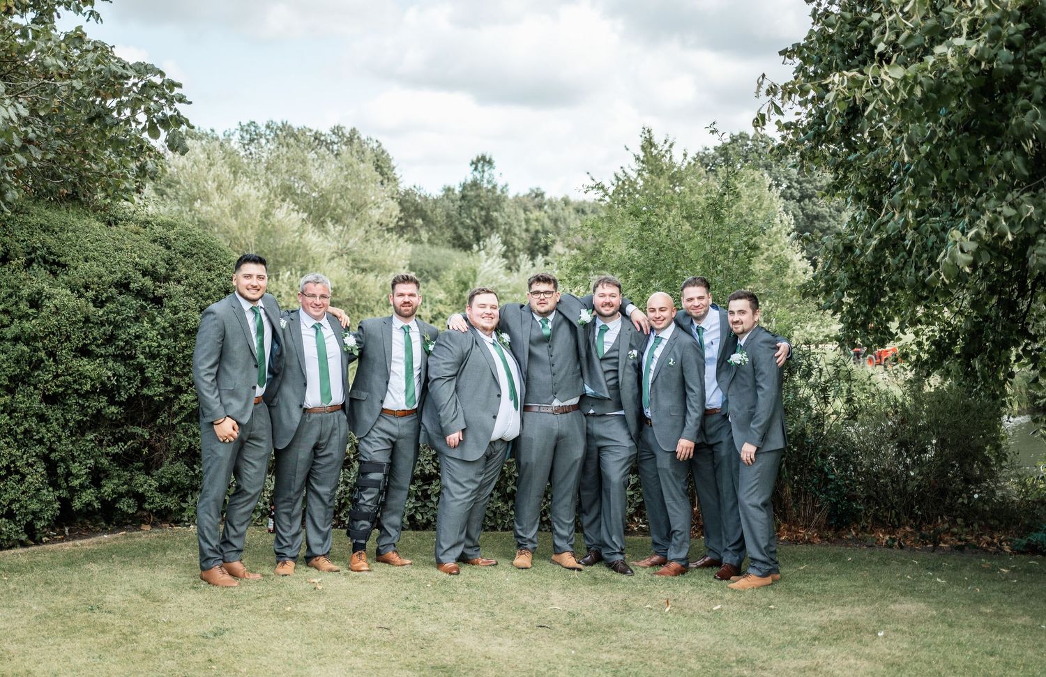 Groomsmen in gray suits pose together on green lawn for group photo.