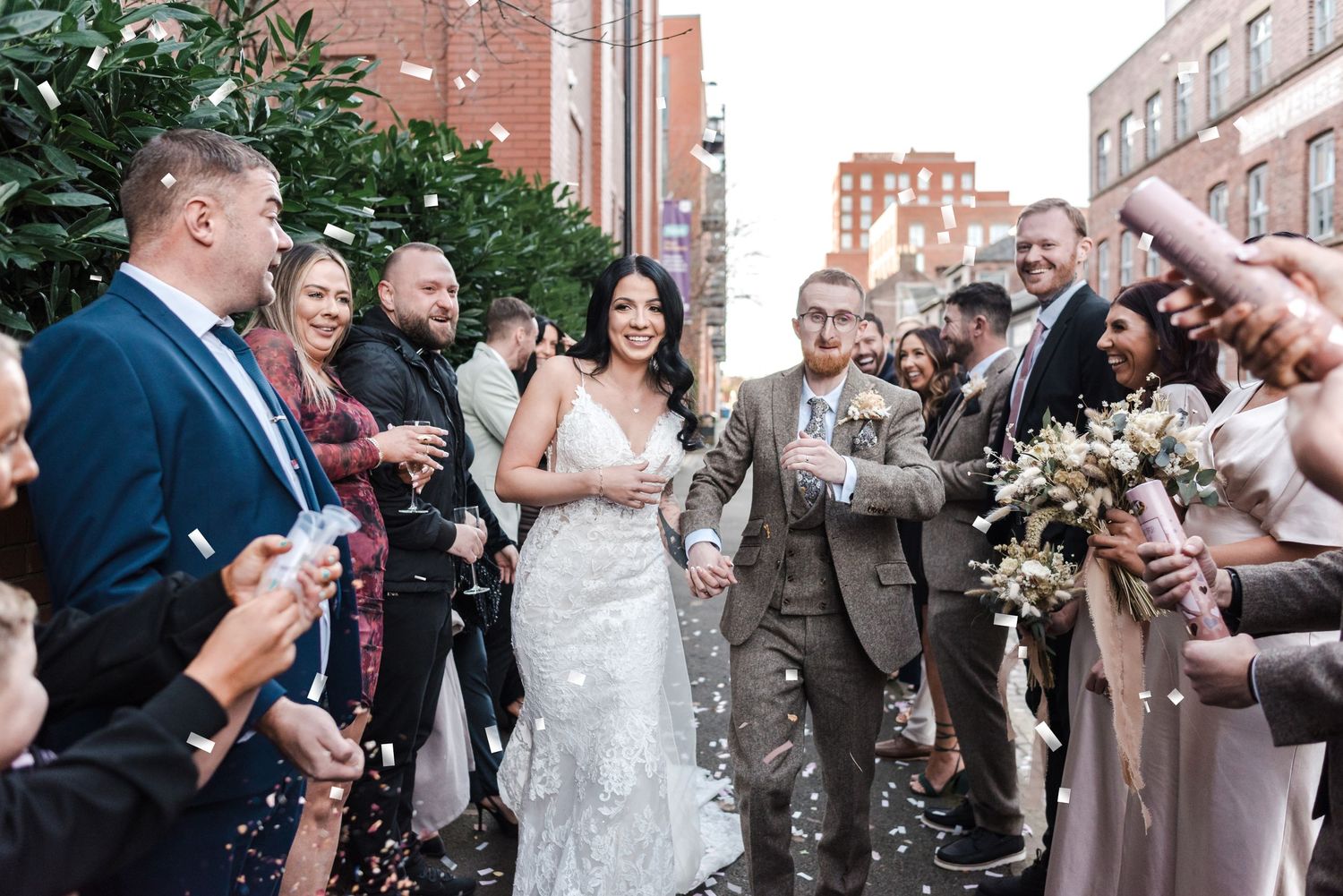 Wedding guests throwing confetti at newlyweds outside brick building.