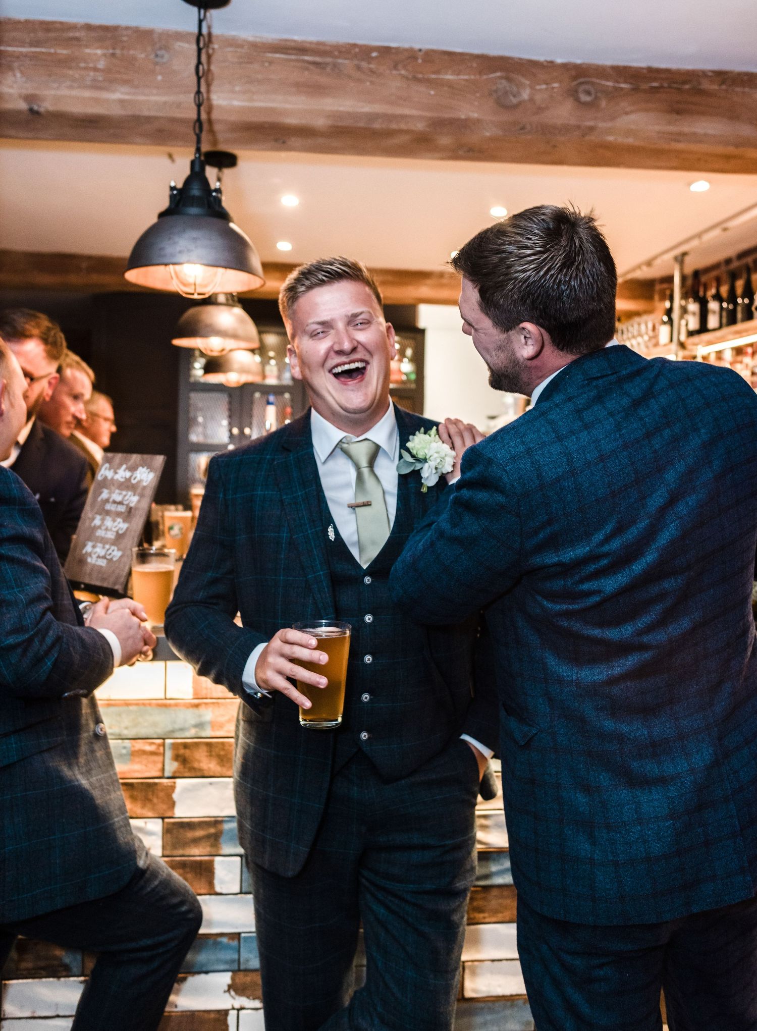 Guests sharing laughs and drinks at wedding reception bar area.