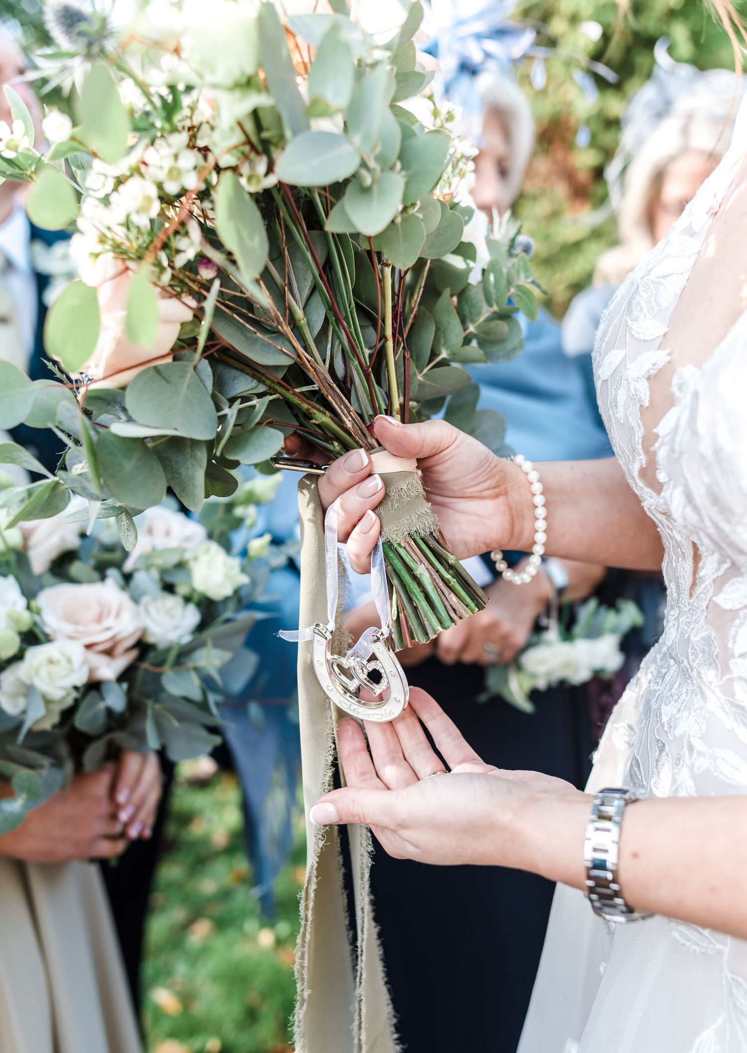 Close-up of bridal bouquet with eucalyptus leaves and white flowers tied with decorative charm.