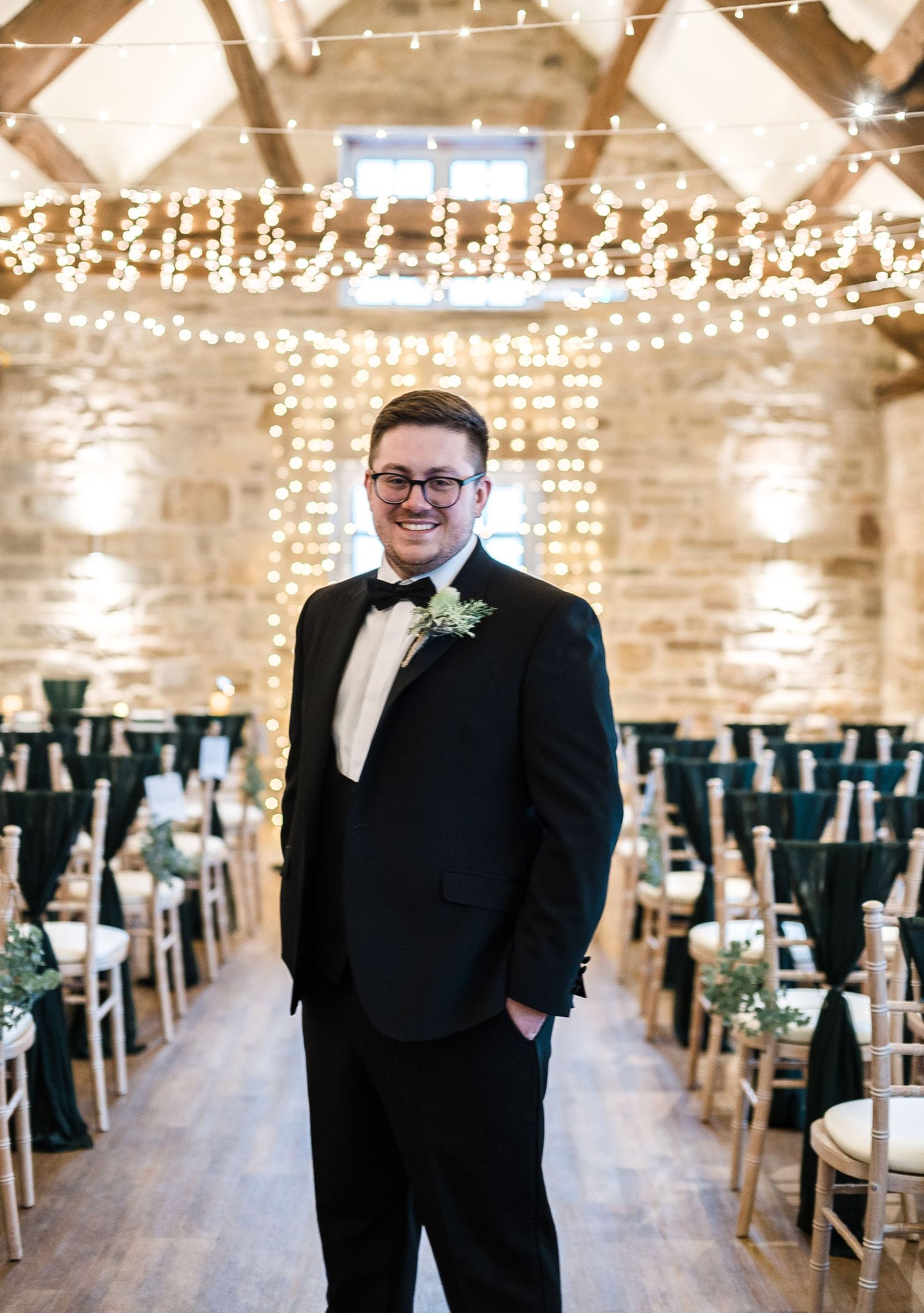 Wedding ceremony venue with twinkling lights and rows of teal chairs in a rustic stone barn setting.