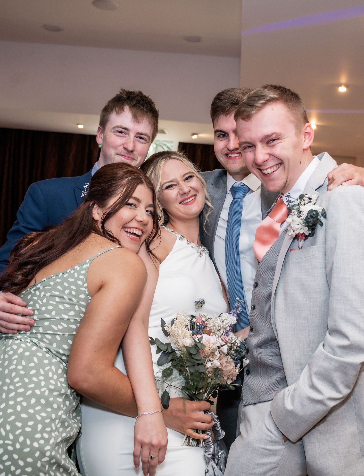 Wedding party shares a joyful moment together with bride wearing white dress and holding floral bouquet.