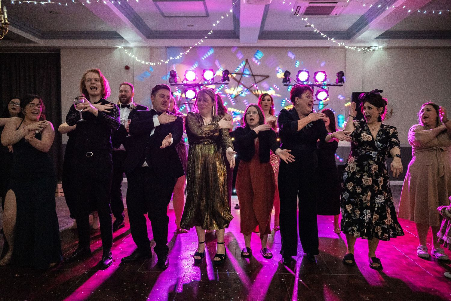 Wedding reception guests dancing under purple lighting with festive decorations.