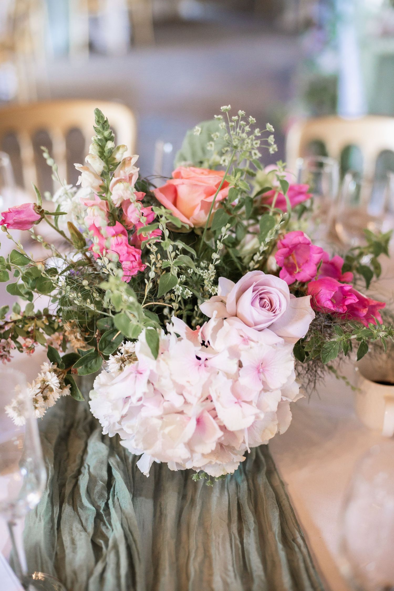 Elegant floral centerpiece with pink roses and hydrangeas on sage green table runner.