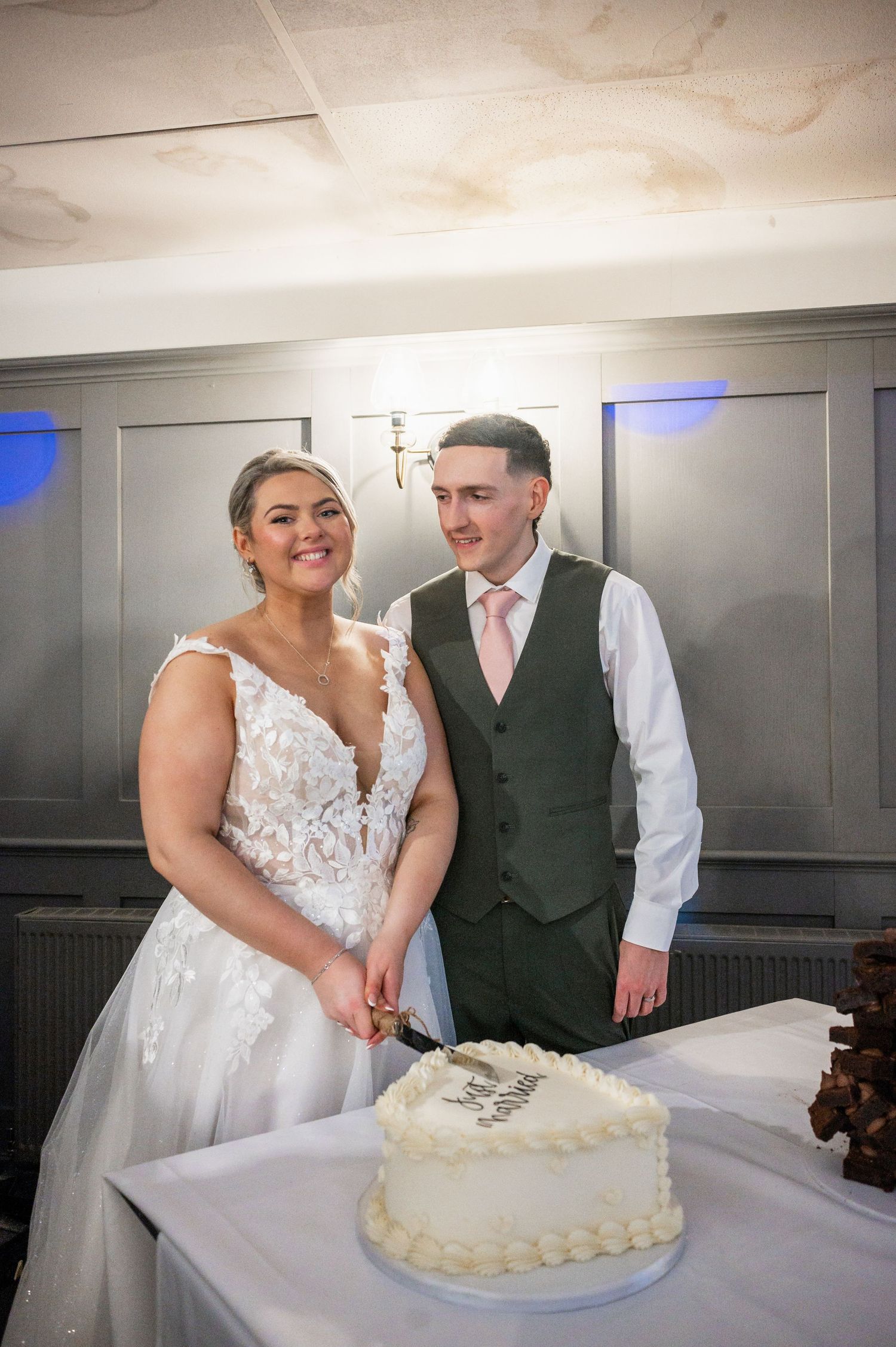 Couple standing by their white wedding cake during their reception celebration.