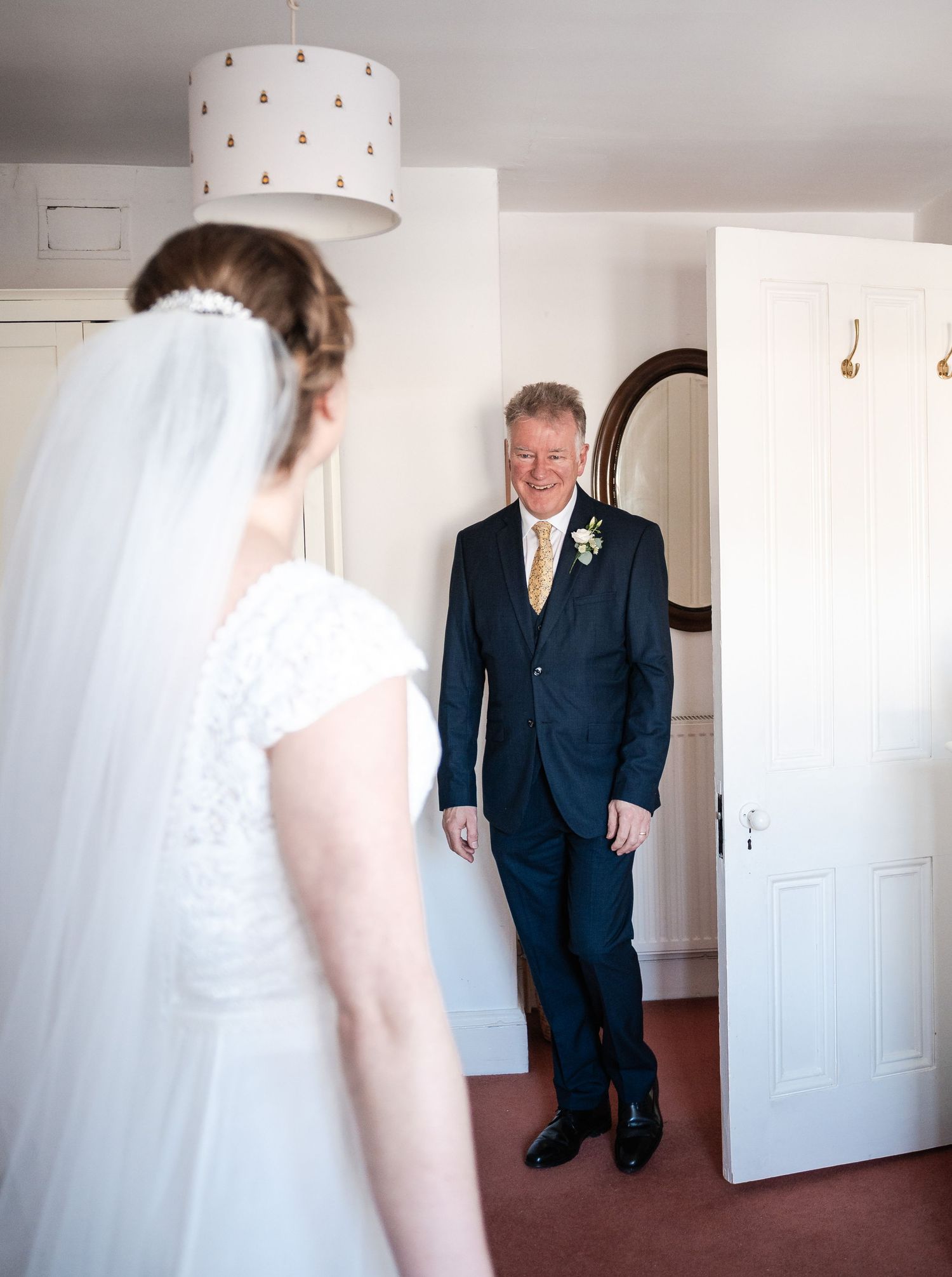 A touching first look moment between a bride in white and a person in a dark suit in a bright indoor setting.