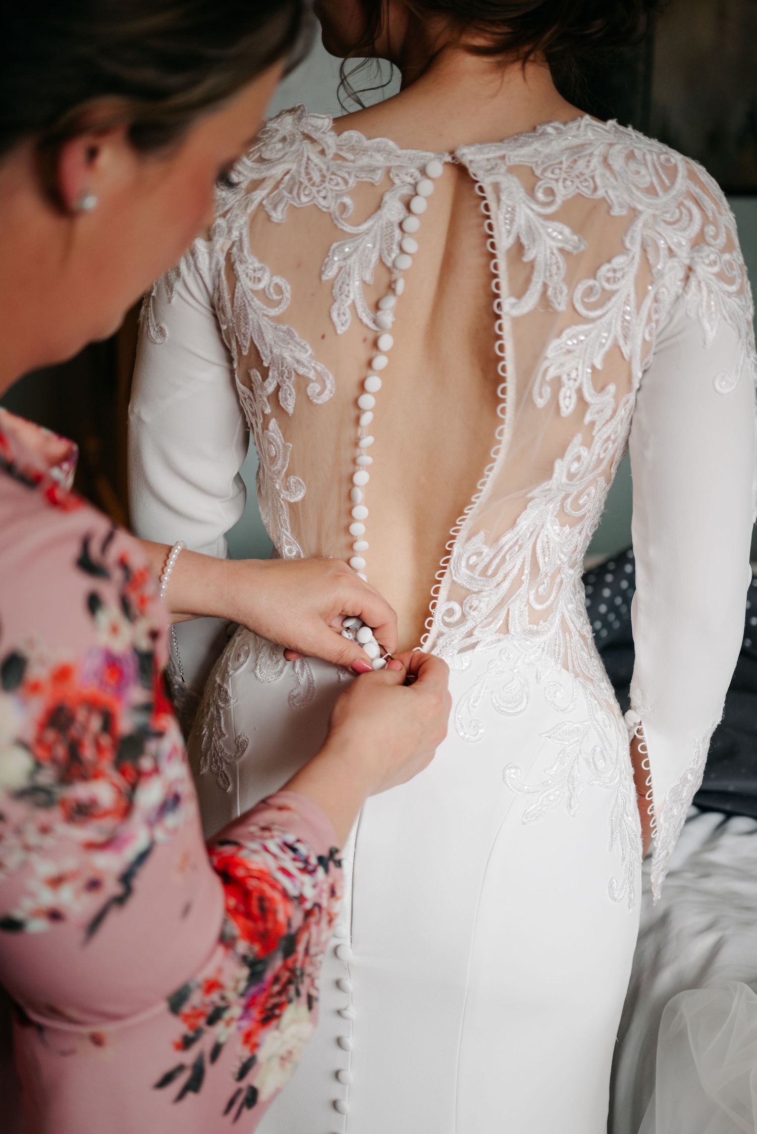 Close-up details of a white lace wedding dress with delicate button closures and sheer back panel.