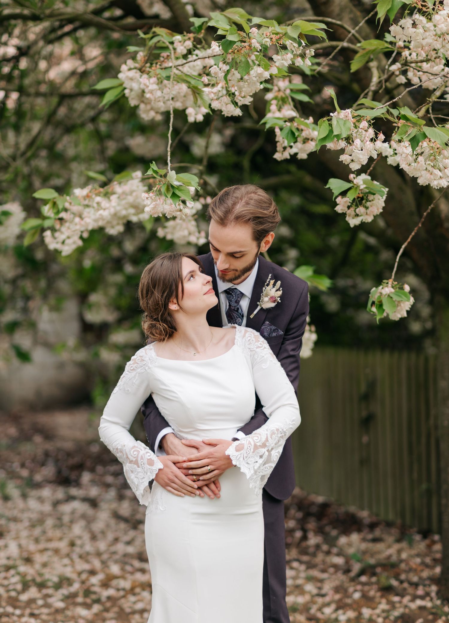 Romantic wedding photos under blooming spring tree branches with delicate white flowers.
