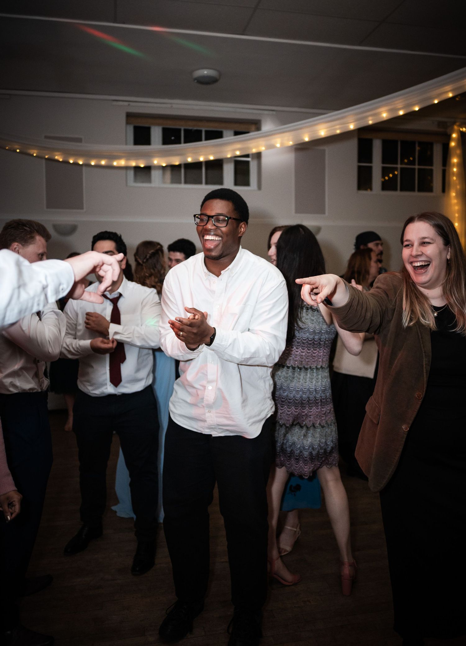 Wedding guests dancing and celebrating under string lights at an indoor reception.