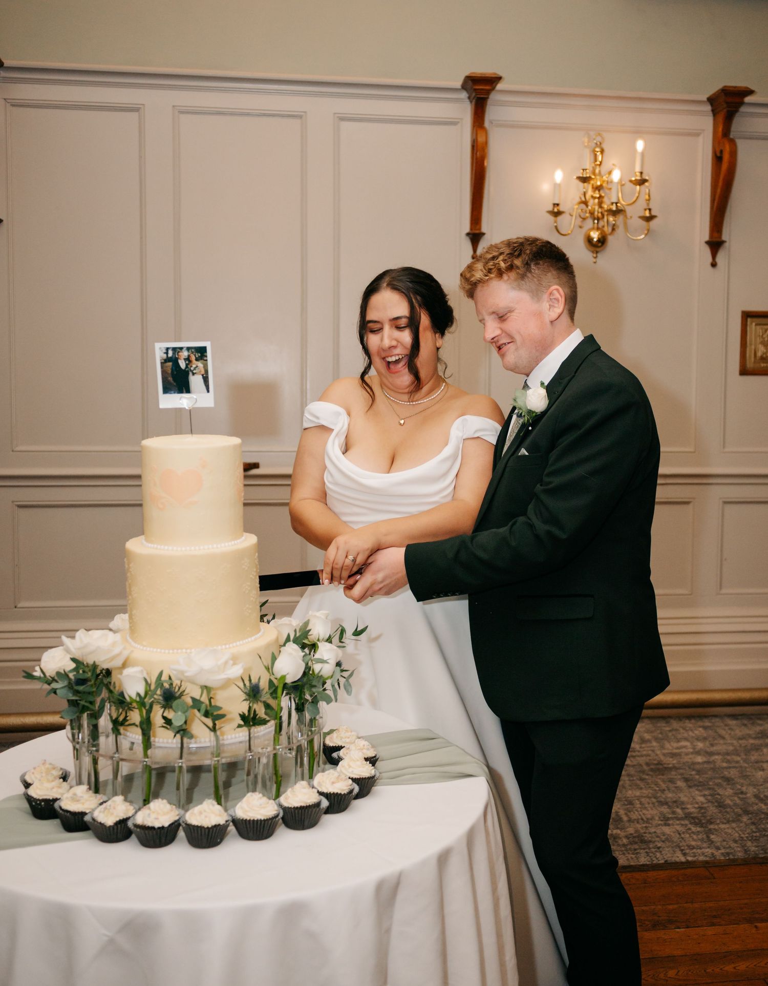 Wedding cake cutting ceremony with a classic white tiered cake and cupcakes on an elegant display table.