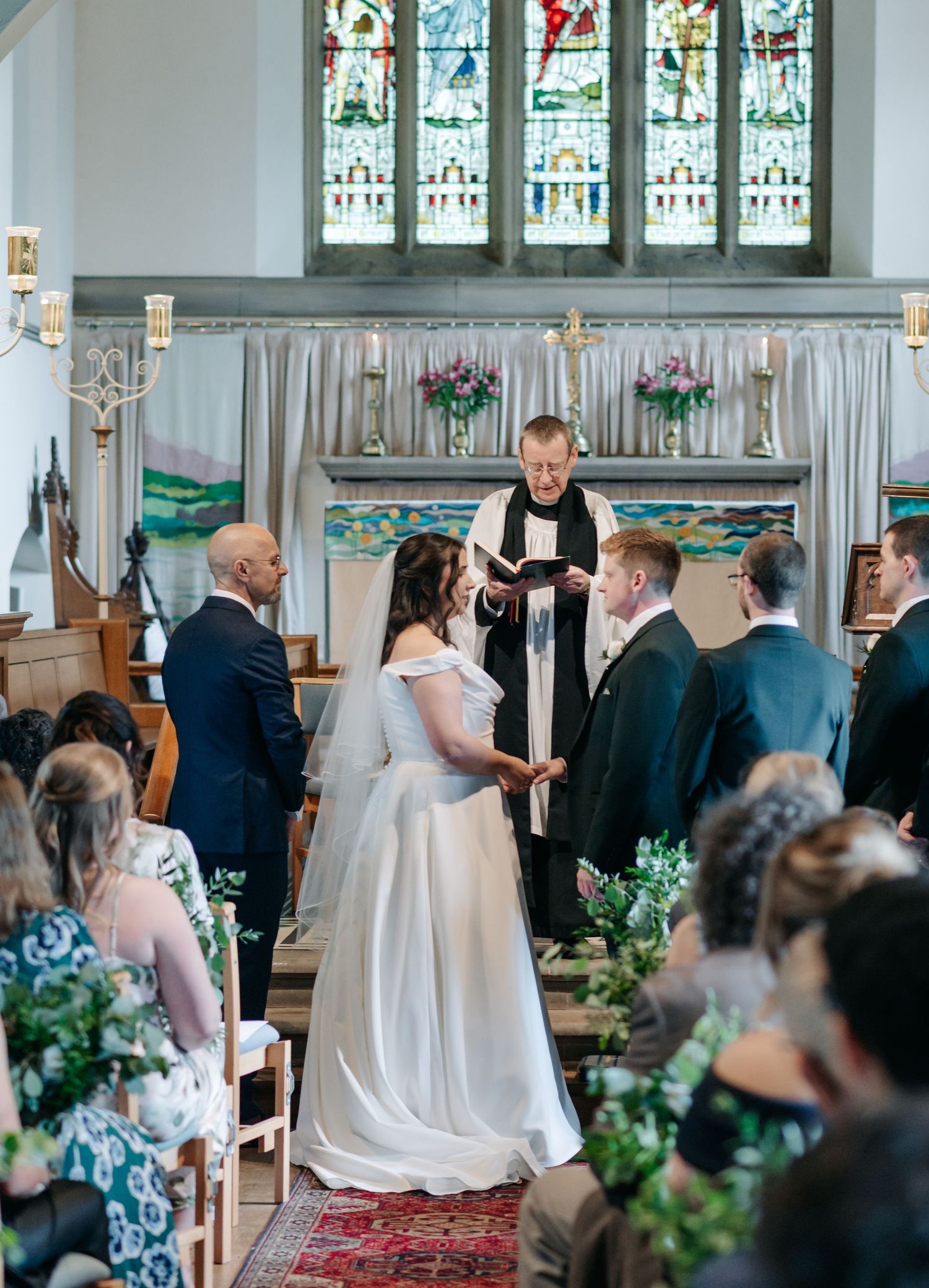Church wedding ceremony with stained glass windows and floral decorations along the aisle.
