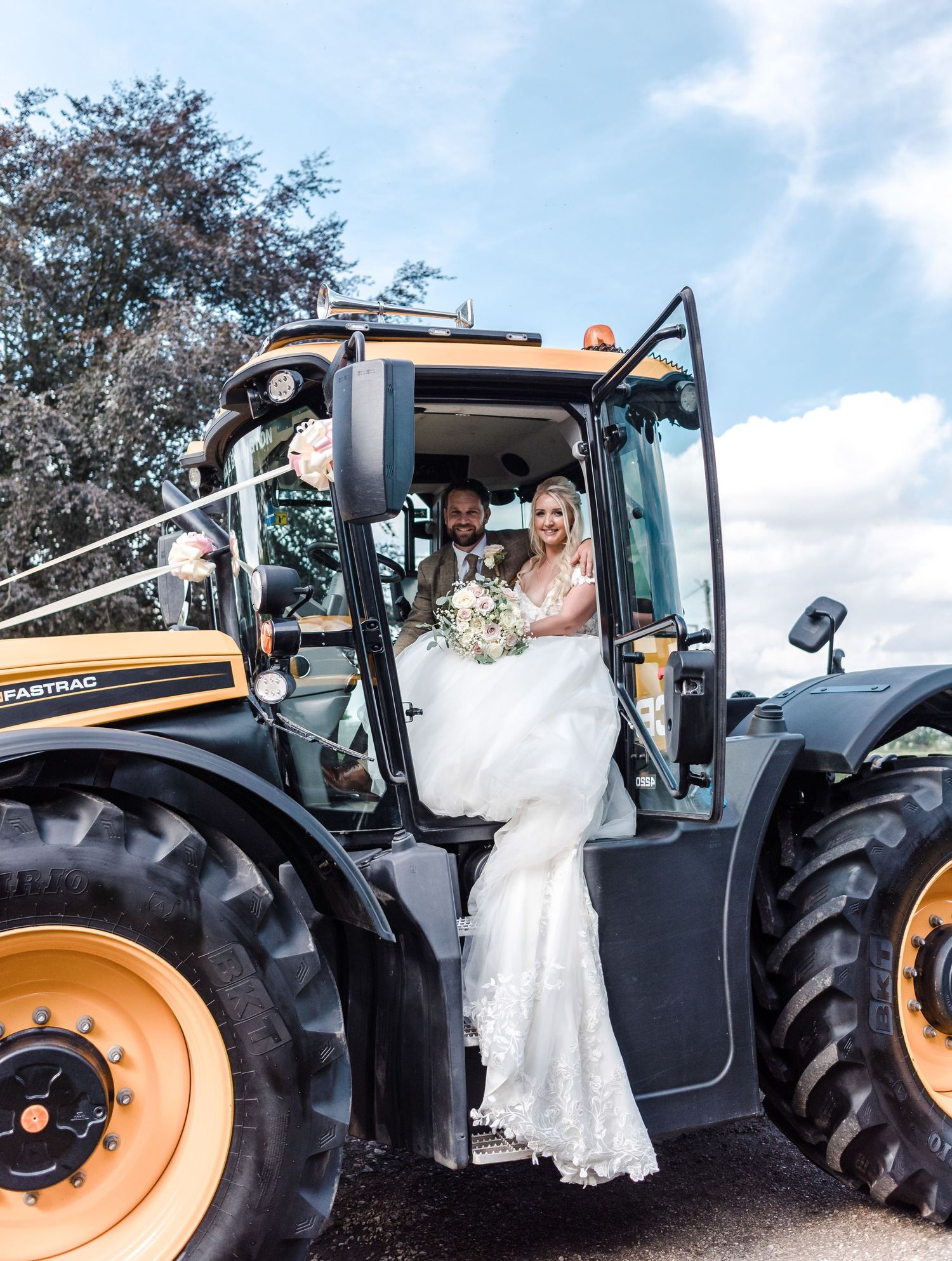 Wedding couple posing in large yellow tractor on their special day.