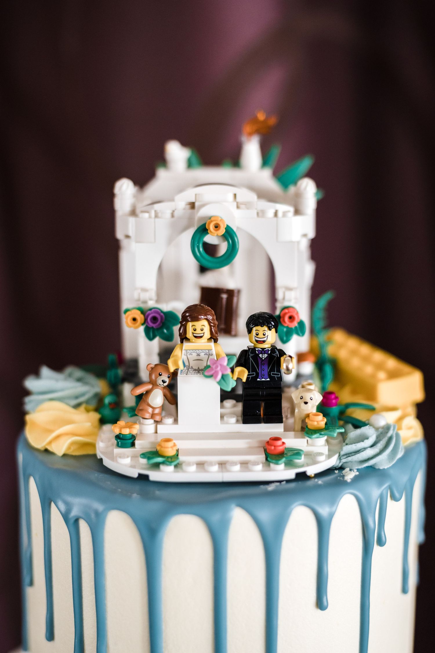 LEGO wedding cake topper featuring bride and groom figures on blue drip-decorated cake.