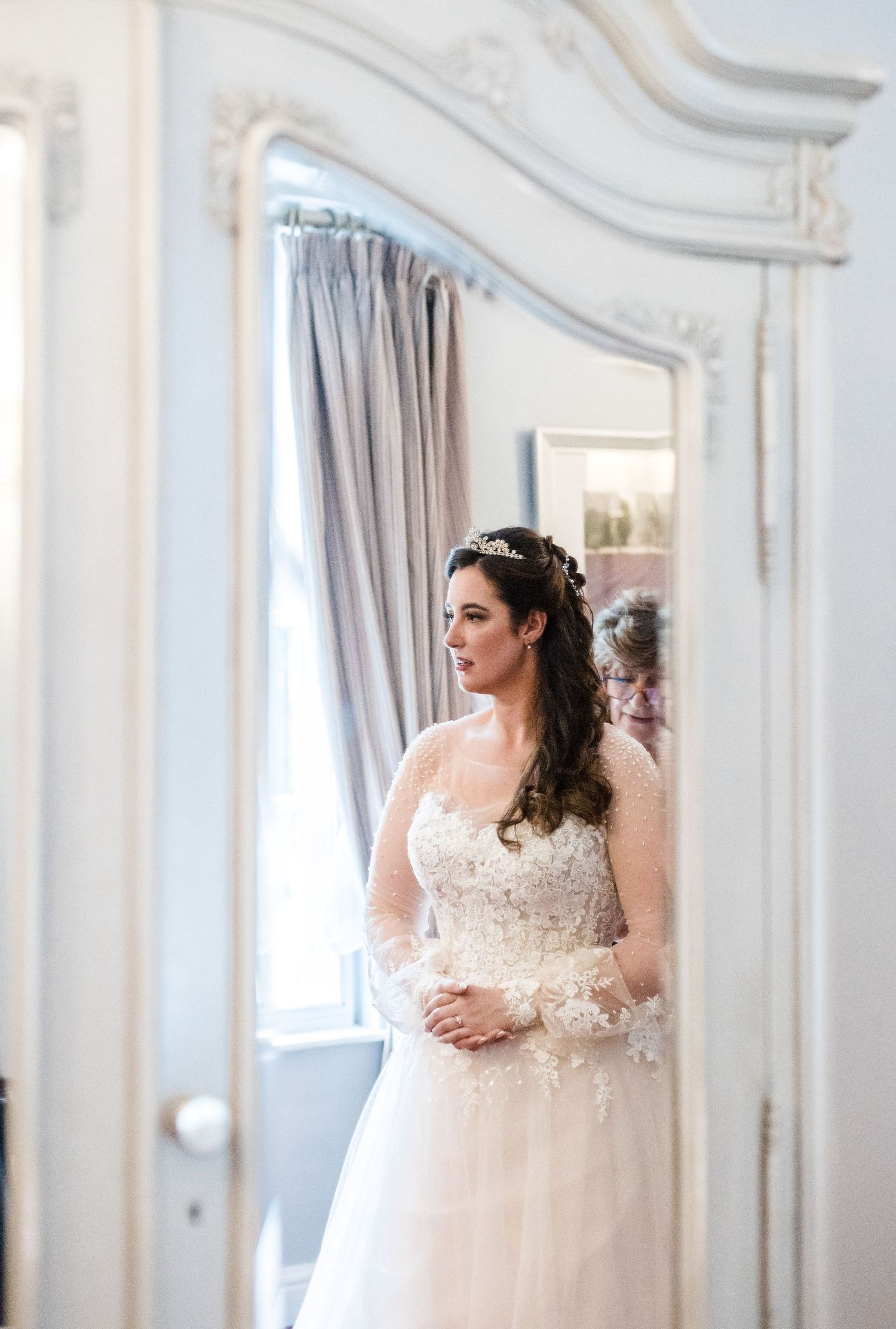 Elegant bridal portrait in front of ornate white mirror and curtains.