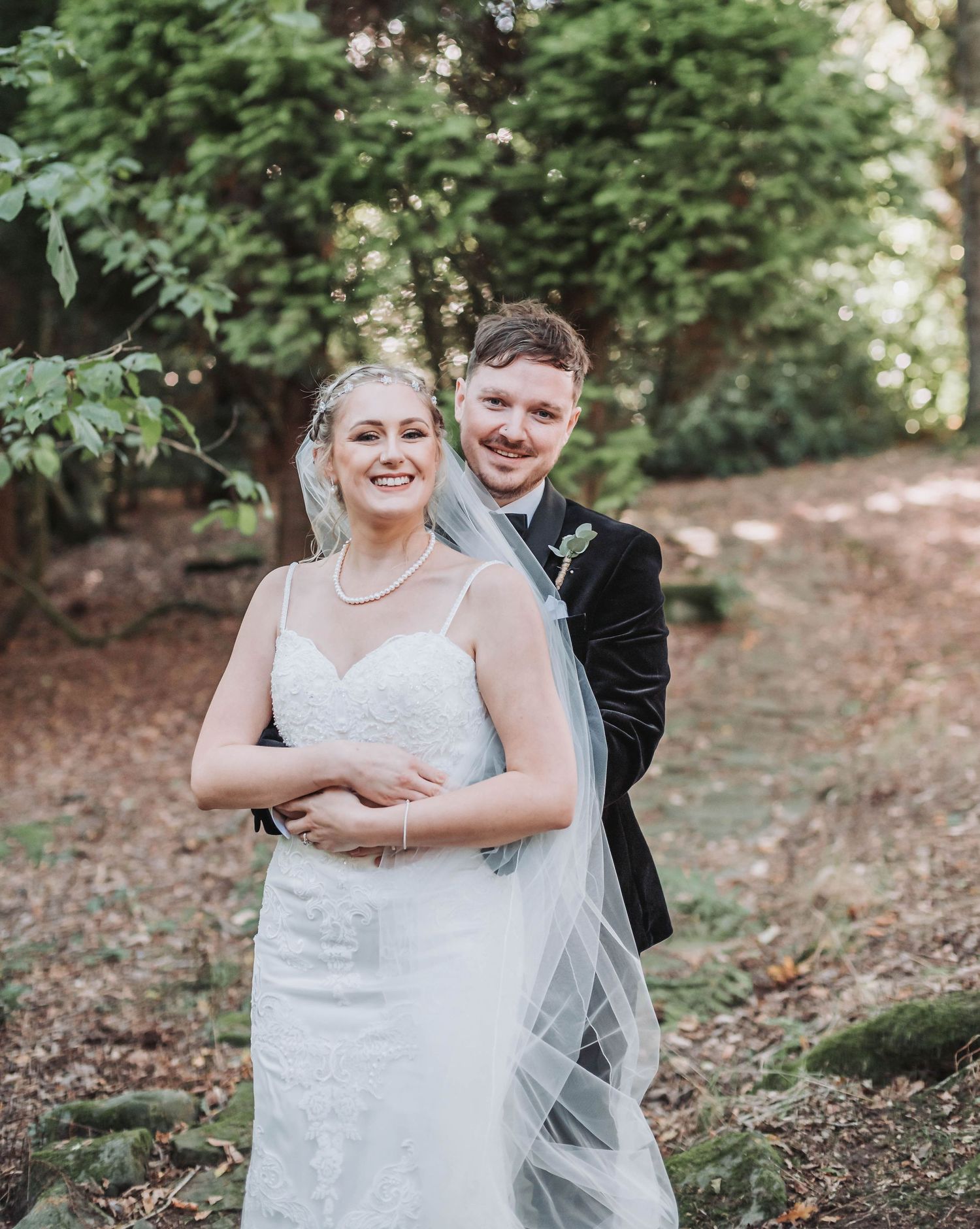 Joyful wedding couple embraces while posing for portraits in a scenic woodland setting.
