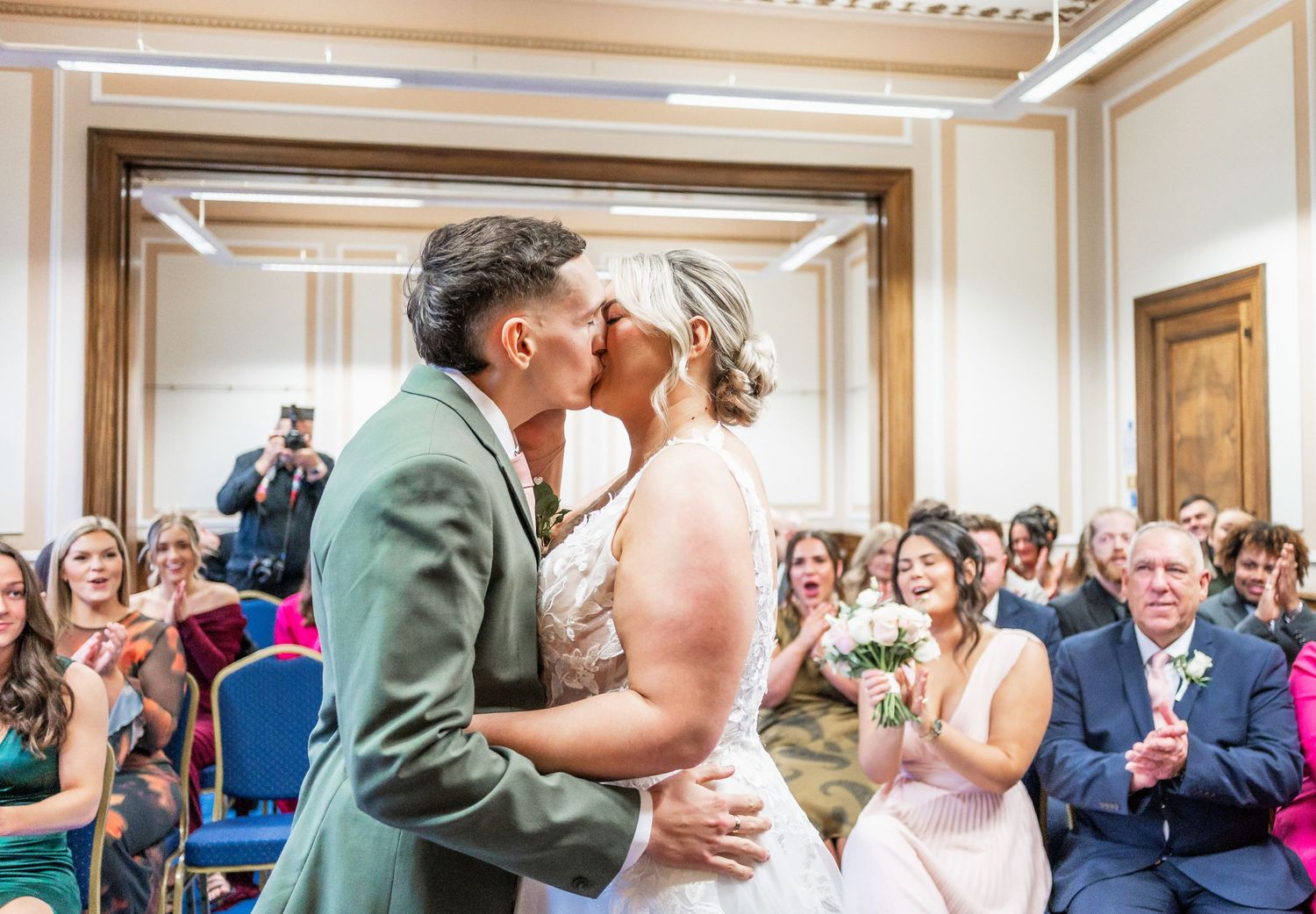 Celebratory kiss during wedding ceremony with guests applauding in the background.