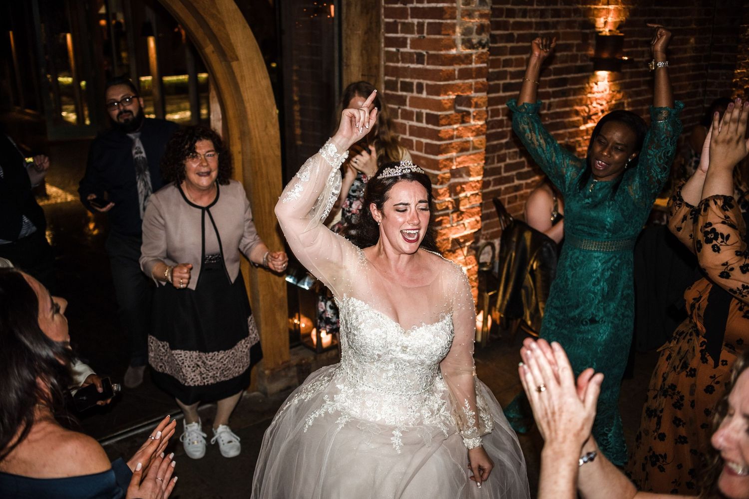 Celebration on the dance floor with guests dancing in front of exposed brick walls.