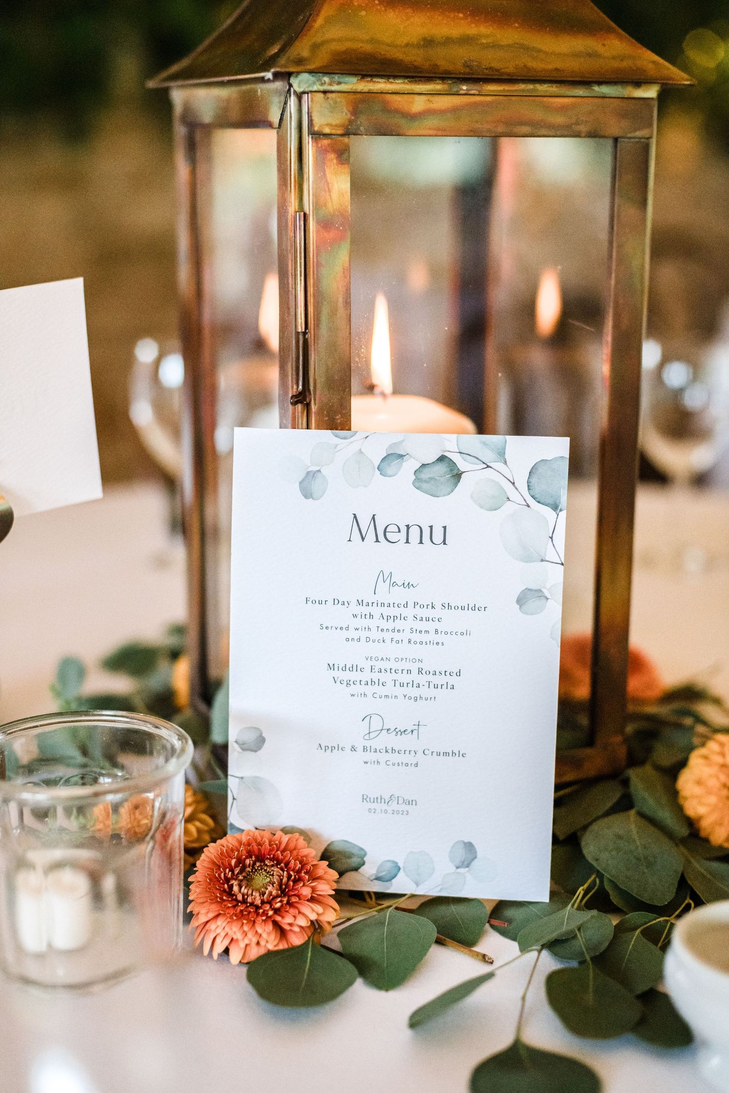 Rustic wedding table decor with lantern centerpiece, menu card and coral flowers.