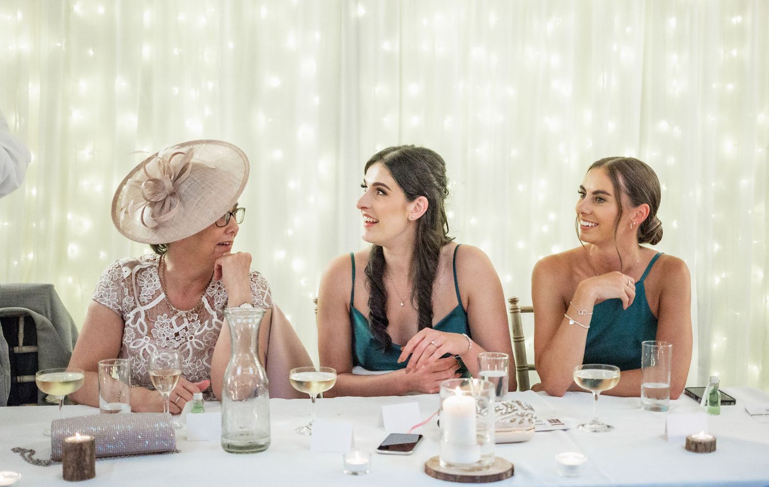 Wedding guests in formal attire sharing laughs at reception table.