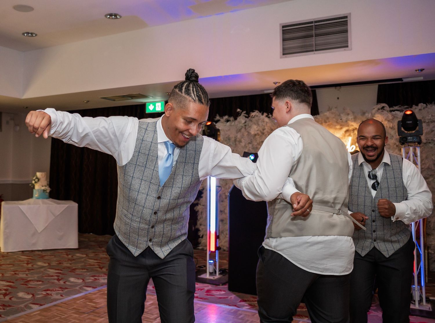 Wedding guests dancing and celebrating at a reception with colorful lighting.