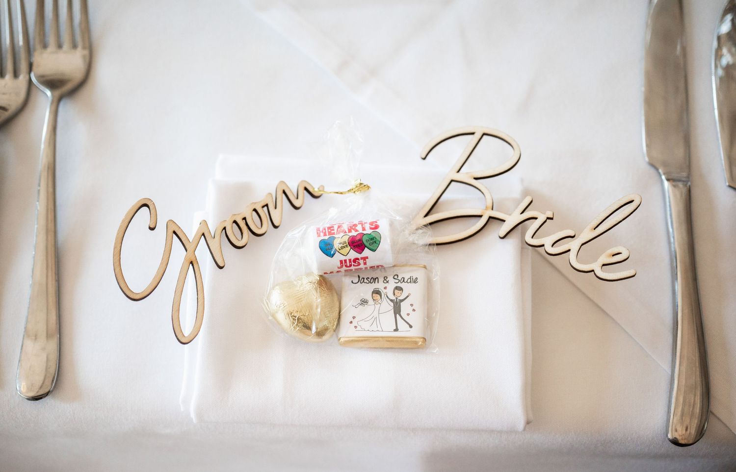 Gold 'Groom' and 'Bride' place settings with delicate floral accents on white tablecloth.